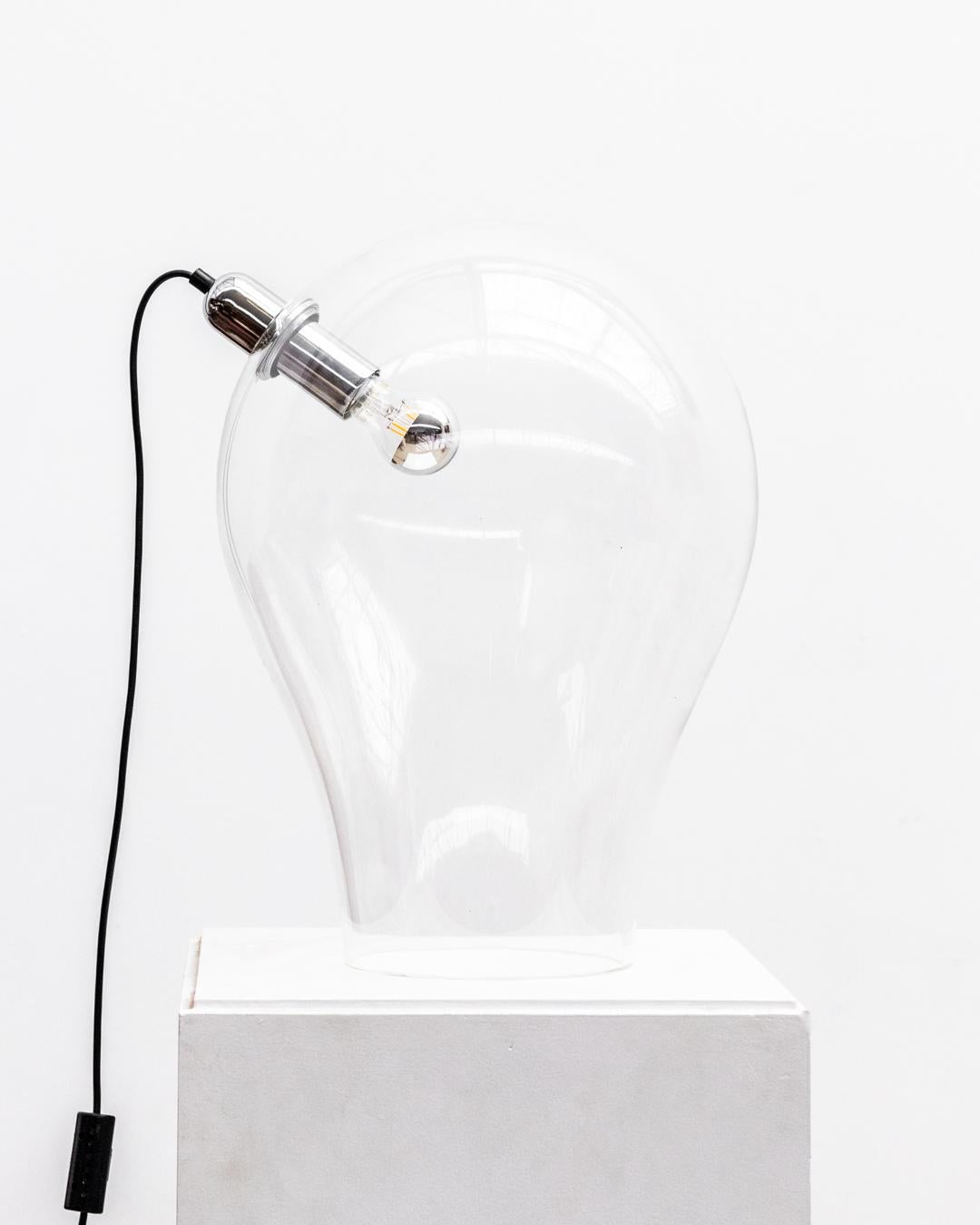La lámpara de escritorio minimalista de cristal XL con una fuente de luz rodeada de acero inoxidable, editada por Lumenform en la década de 1970, representa una mezcla por excelencia de  diseño moderno y elegancia funcional caracterizados por líneas