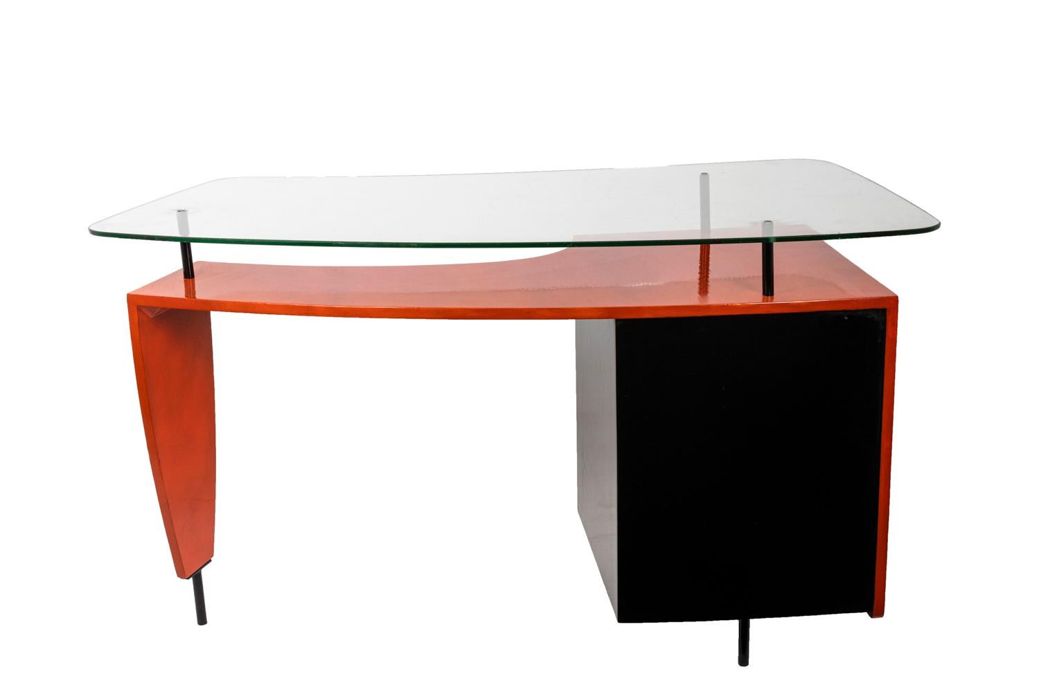 Left compartment desk in black and orange lacquered wood opening by four drawers. The desk stands on three black lacquered metal legs. The first orange lacquered half-moon-shaped tray is topped by a curved glass tray standing on three black