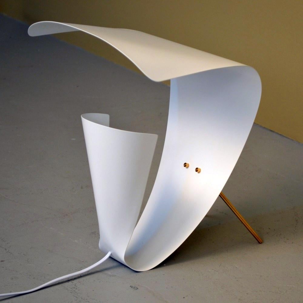 Distinctive and playfully expressive, this desk lamp, like the sconce, hides the bulb in a curved base that also serves to project the light. However, additional curves on top catch the light and focus it back down. Fixed brass legs in the back keep