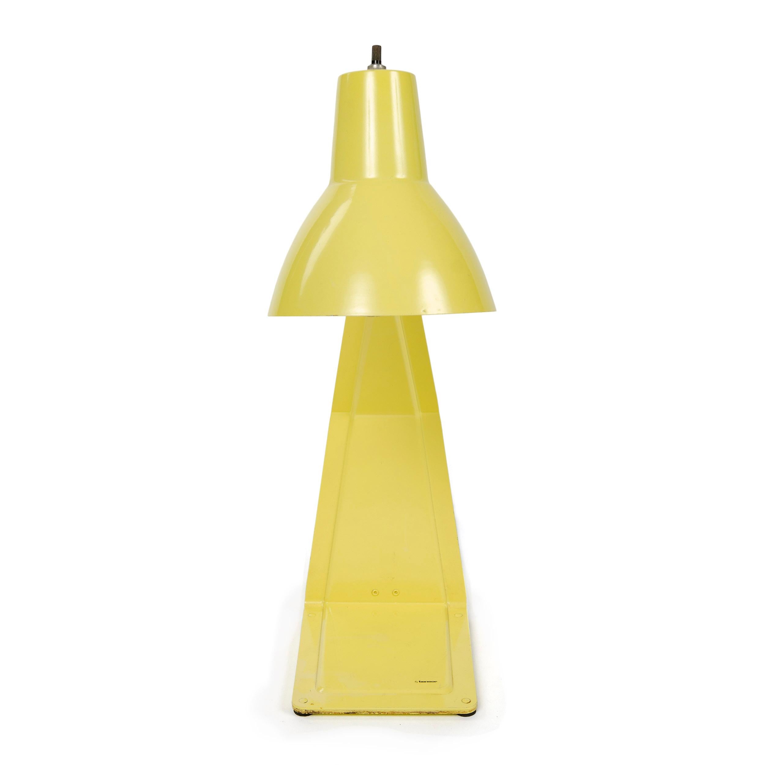 A desk or table lamp made of a singular stamped, die cut and folded piece of metal, painted yellow with a pivoting shade.