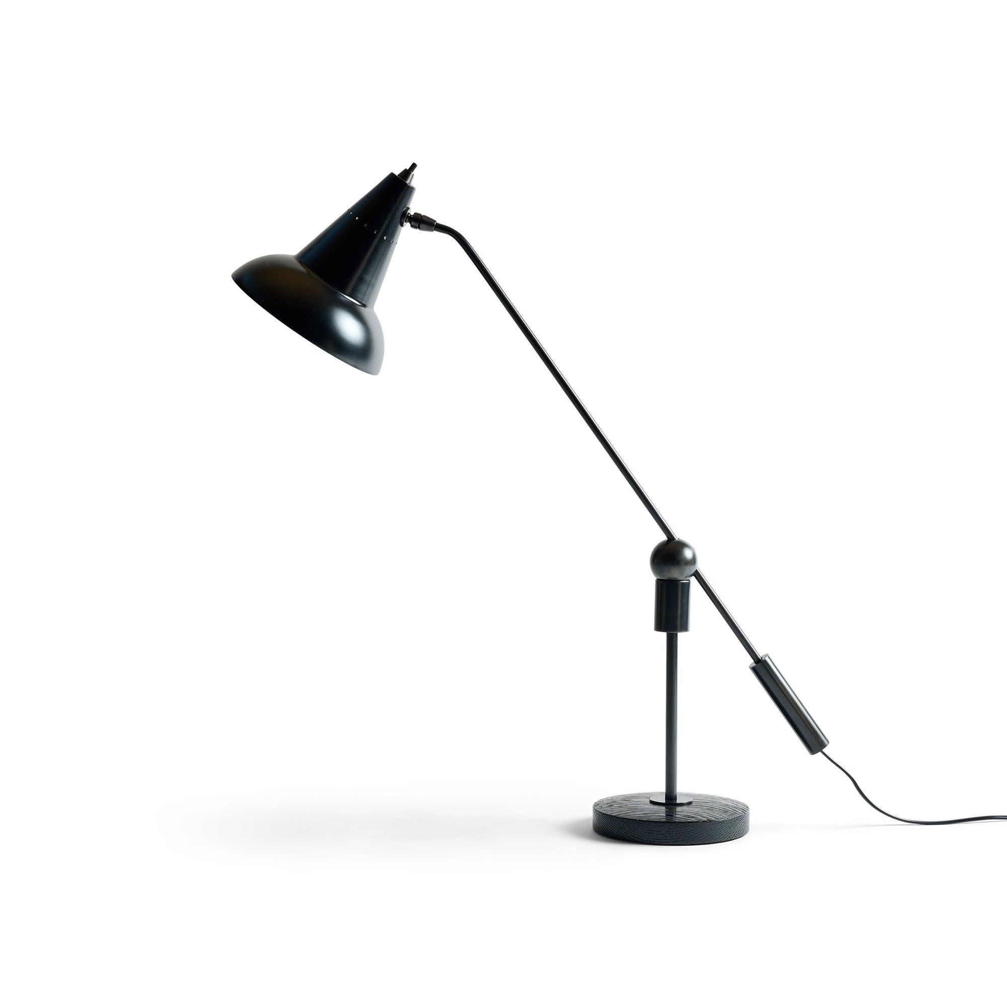 Eine schwenkbare Schreibtischlampe mit einem kegelförmigen Schirm auf einem runden Holzsockel und einer magnetischen Kugelverbindung, die die Bewegung ermöglicht.