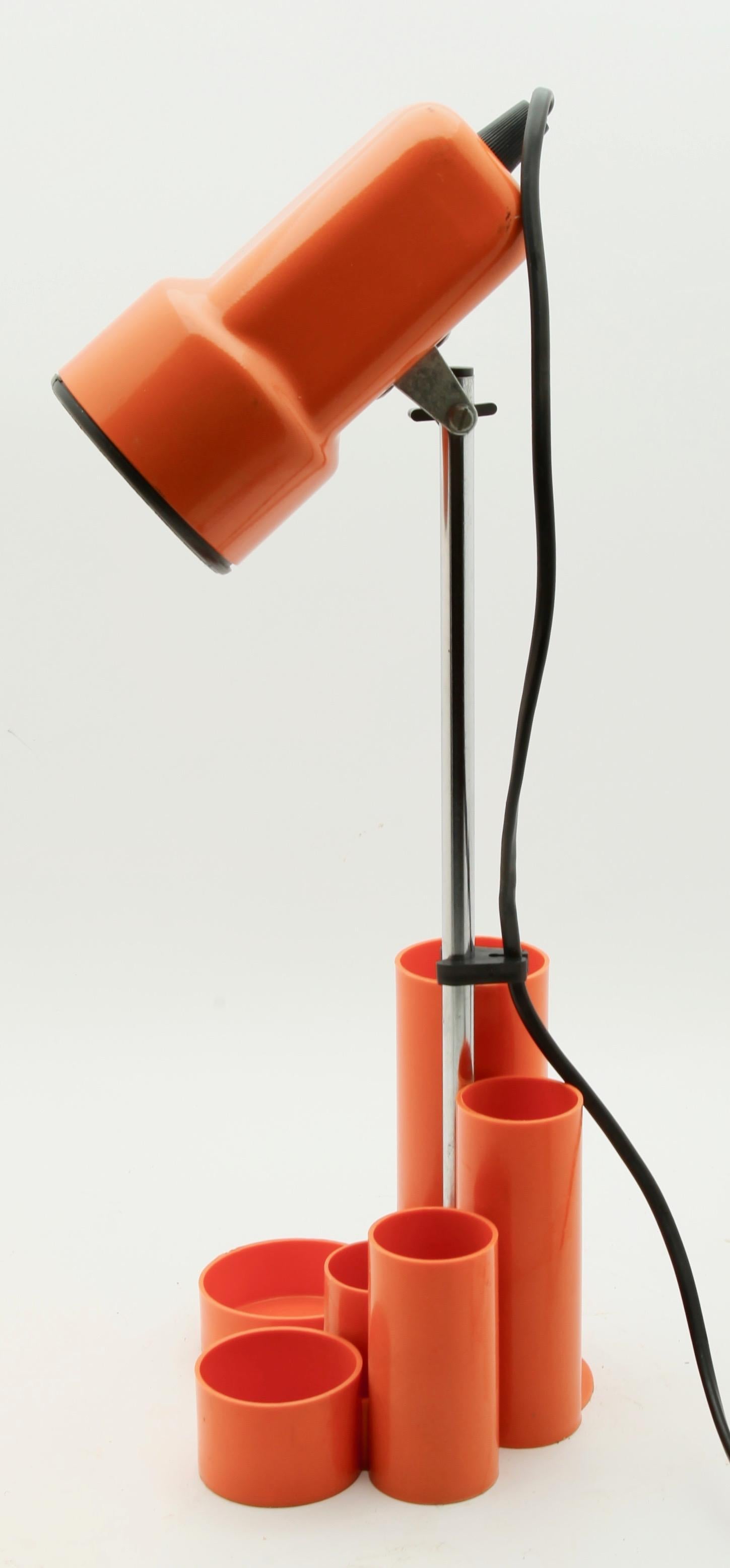 A bright and simple desk-tidy provides the base for a small spotlight, ensuring maximum functionality in minimum space. Typical of the 1960s it's funky orange color gives your desk a hit of period color.
There is space for pens and small items in