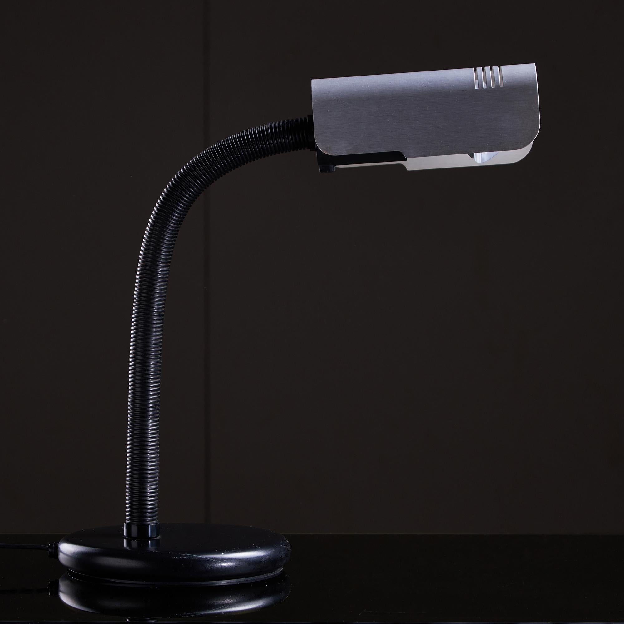 Diese Targetti Sankey-Tischleuchte im Vintage-Stil ist eine scharfe Studie der italienischen Beleuchtung der 1970er Jahre, die industrielle Klarheit mit skulpturaler Absicht verbindet. Das Design besteht aus einem schwarzen Metallsockel mit einer