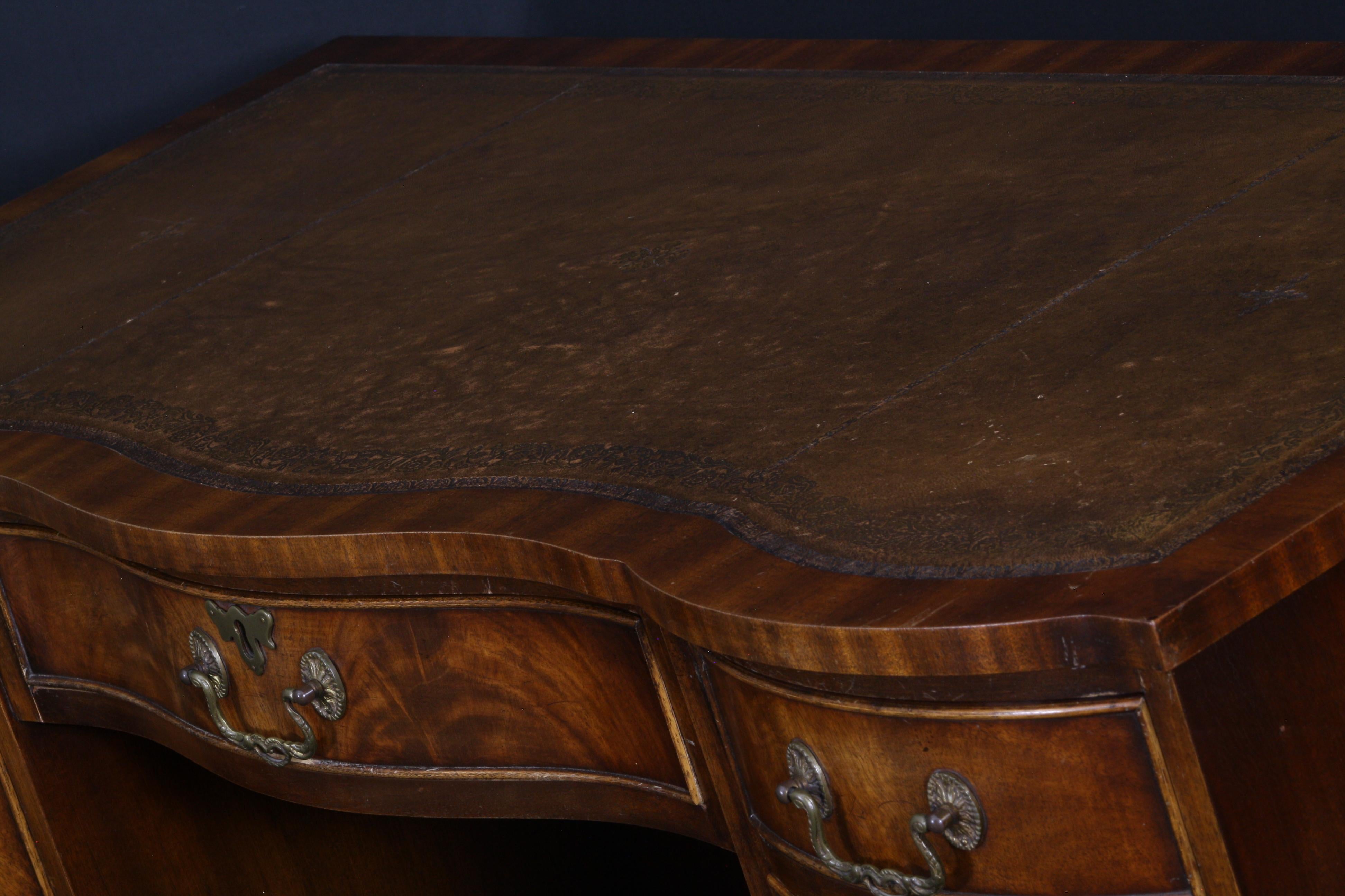 A serpentine curved front, small English kneehole desk in classical mahogany Georgian styling. The goldfish brown tooled leather skiver writing surface embossed with gold tooling has a wonderful patina to it, showing slight use and wear with a minor