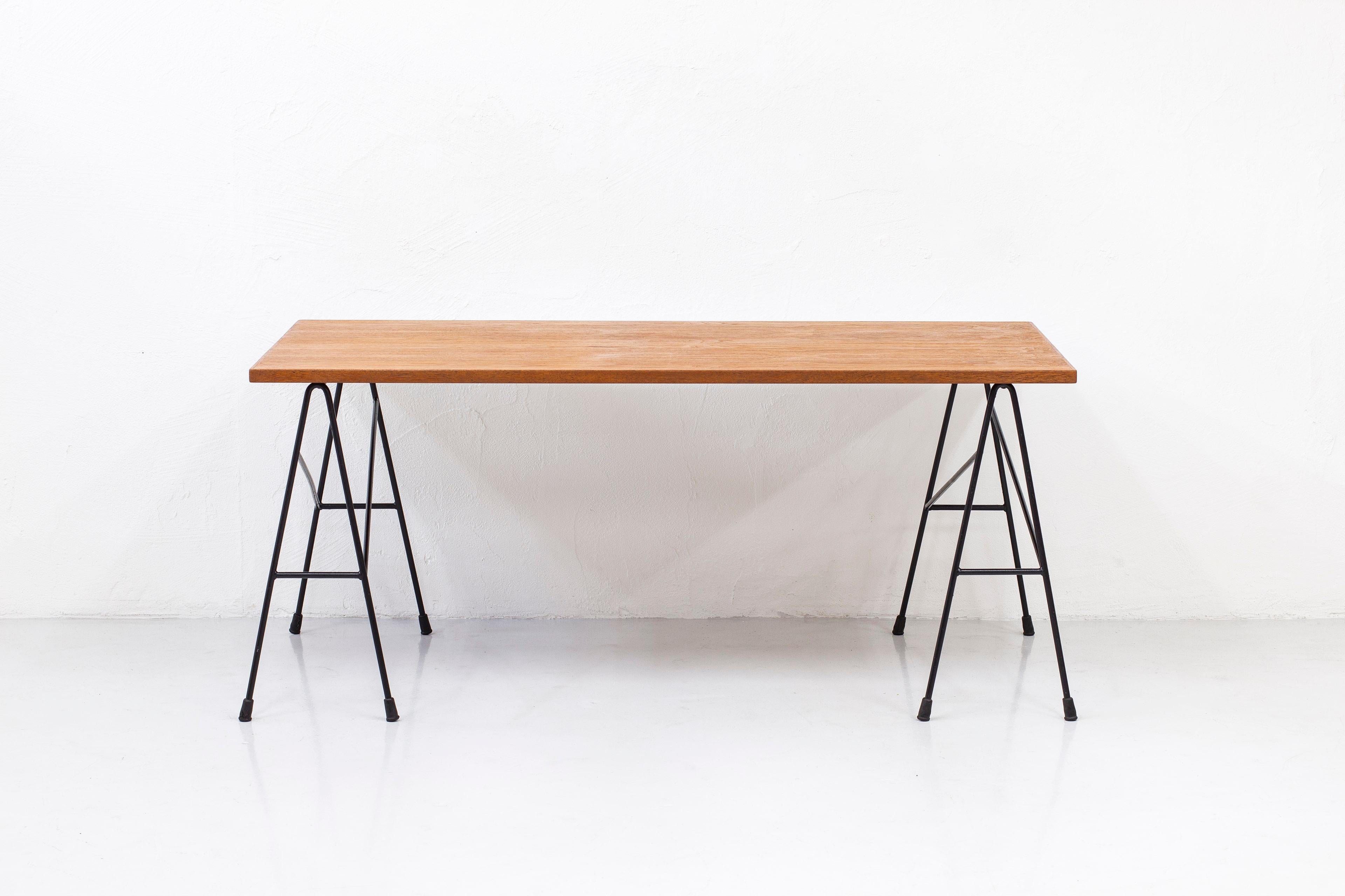 Desk by Bengt Johan Gullberg. Produced by Gullberg trading company in Sweden during the 1950s. Made from black lacquered metal with big rubber feet and table top of teak. Consisting of two metal sawbucks and a loose table top resting on the legs.