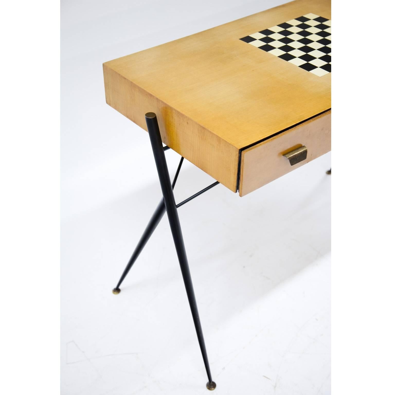 Desk on thin iron legs with one drawer and a chessboard pattern on the top.