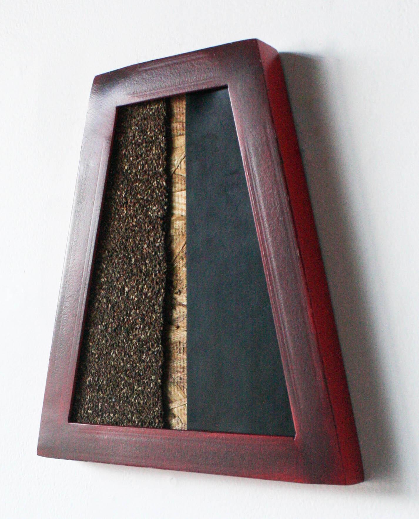 This wall-hanging/wall-mounted sculpture is trapezoidal in shape. Its mixed-media approach yields a variety of textures and colors, from smooth steel to soft rubber and loose graphite. Its mix of red, brown, black, and gray causes it to have the