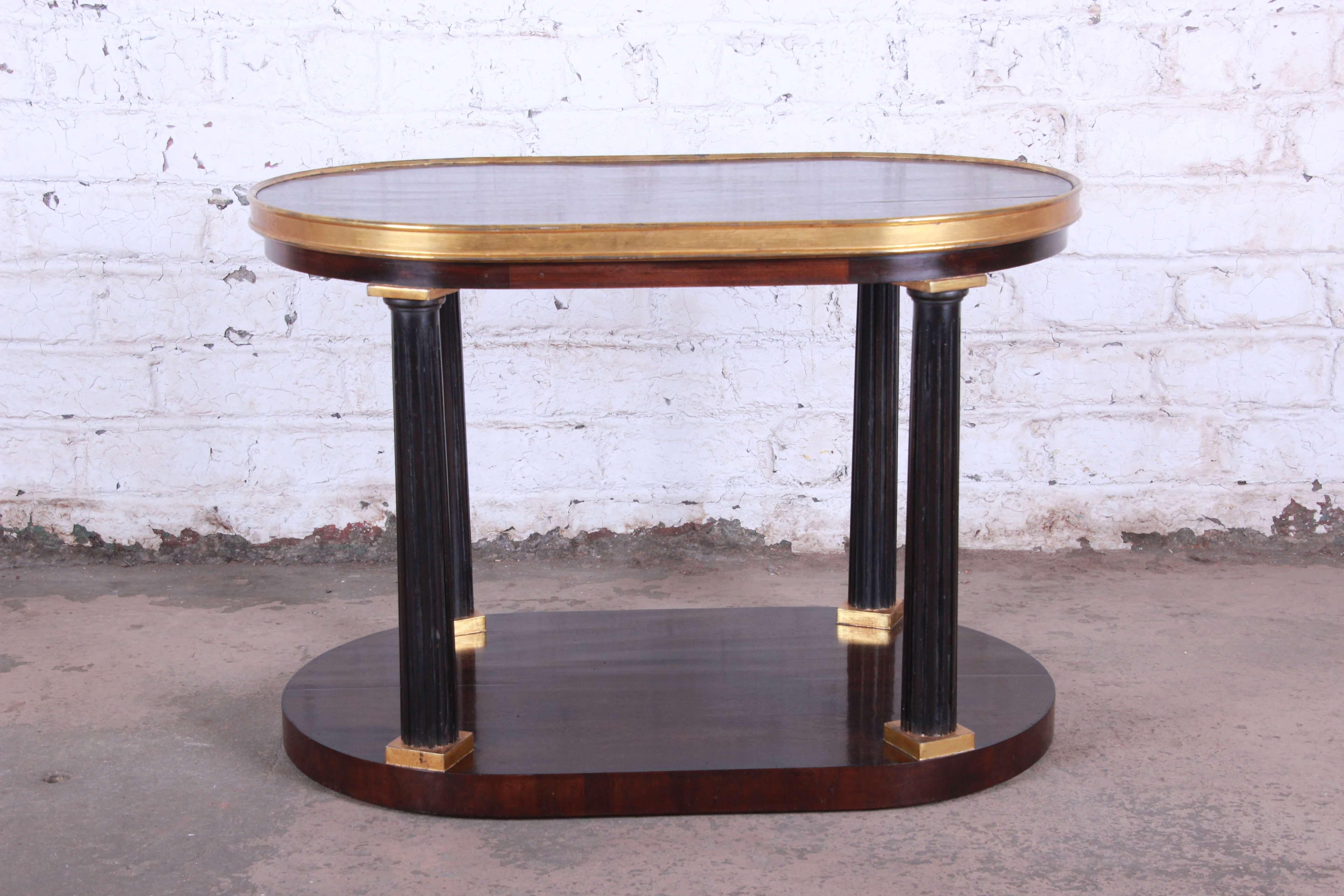 Offering an elegant Dessin Fournir neoclassical oval table. The table has a nice two-tiered design with dark brown shelves. The top has a gilt gold trim with ebonized columns. This very nice table is fit for any important space demand elegance and