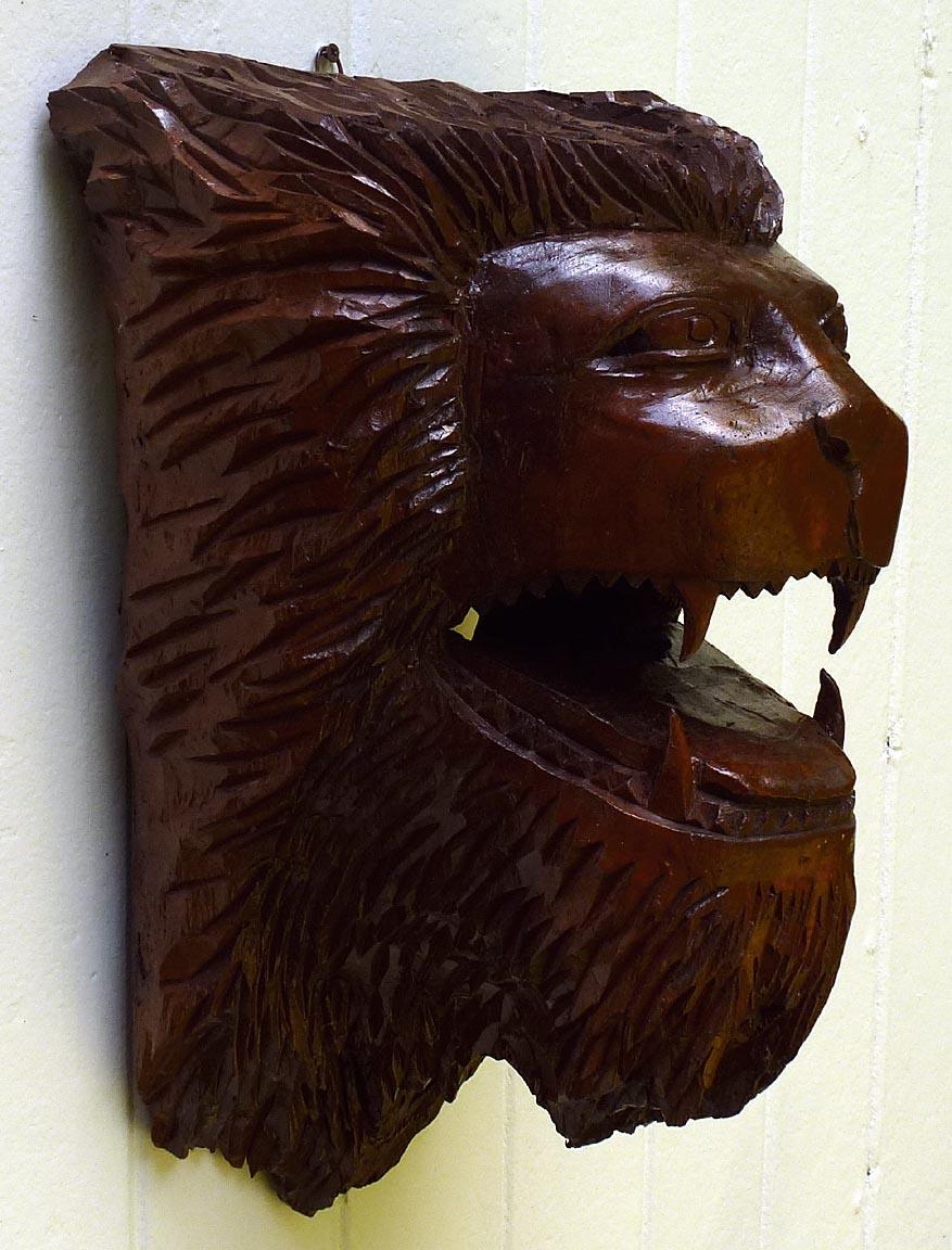 This is a very striking and strong wood carving of a lion's head. It was probably made from walnut, and is finished in a glossy varnish. The carving is quite detailed and extremely impressive. It is approximately 21