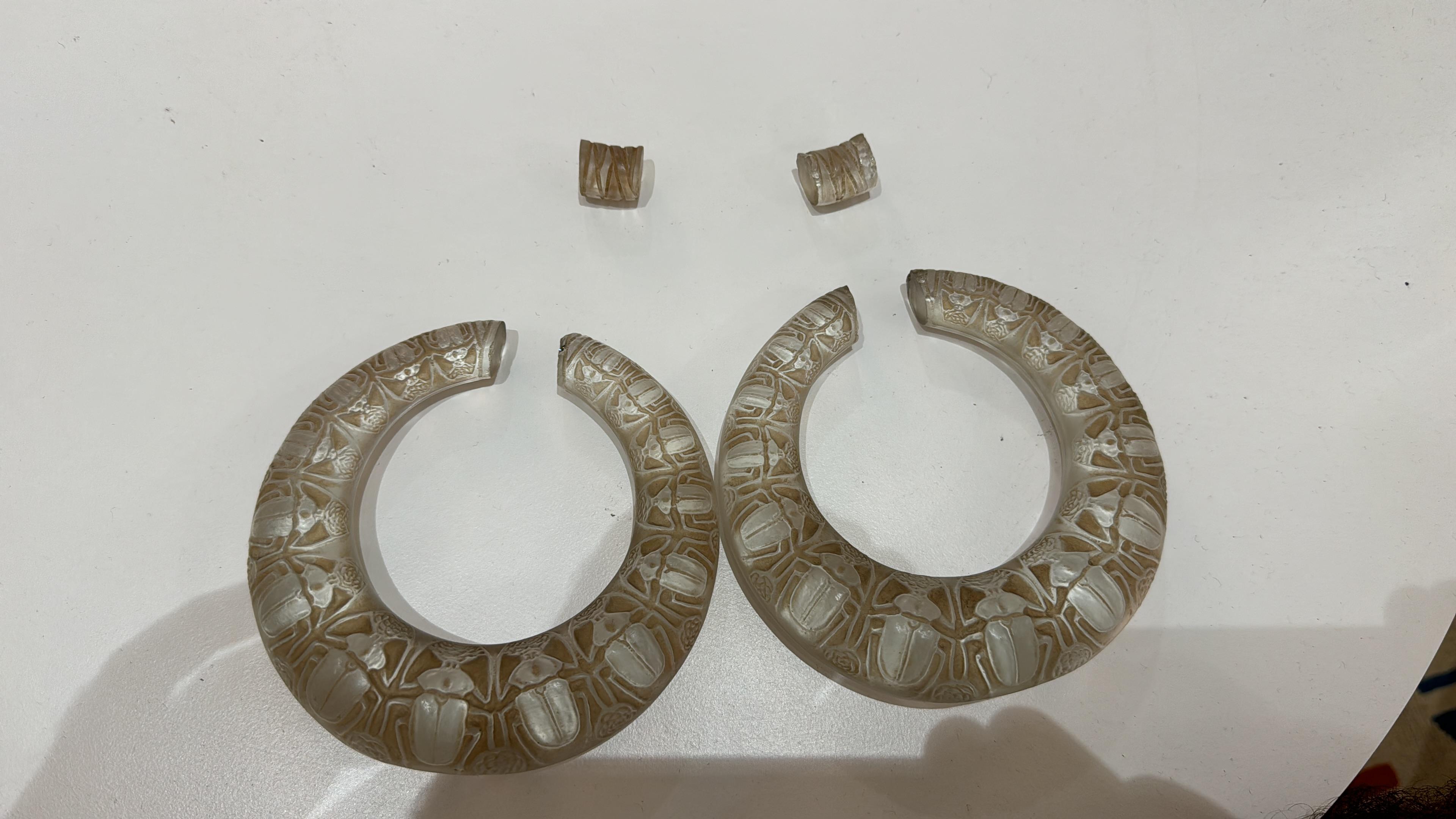 These rare Deux Anneaux Scarabées circular handles were originally designed by René Lalique for his celebrated vase, model no. 882, circa 1919. Crafted in frosted and patinated glass, each ring features the sculpted form of scarab beetles, a motif
