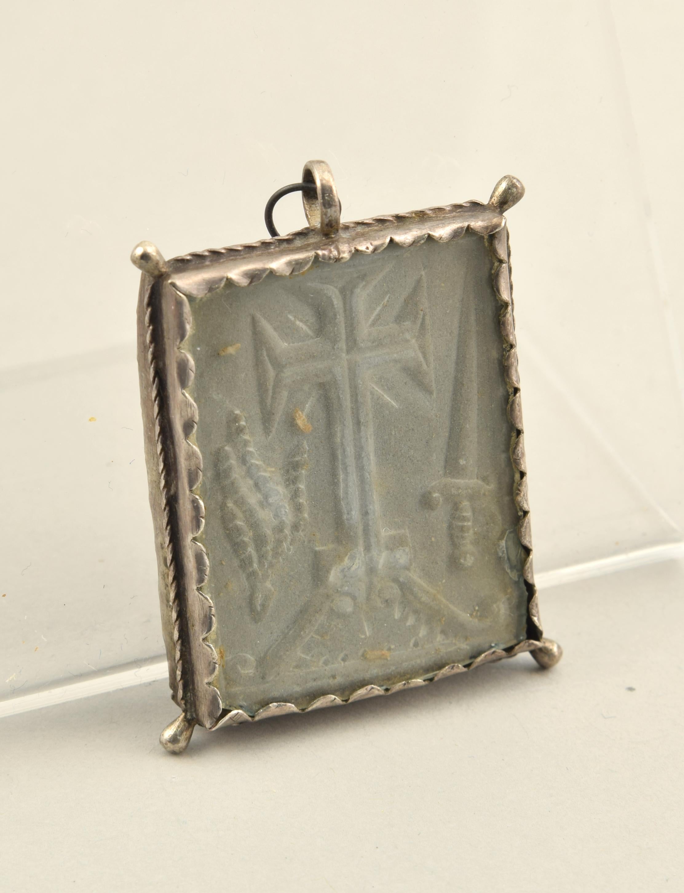 Medal of the Virgen de Nieva with inquisitorial shield. Slate, silver. Spain, 17th century. 
Silver frame.
Devotional medal composed of a silver frame, with corrugations to hold two transparent plates, four pearls in the corners and a ring in the