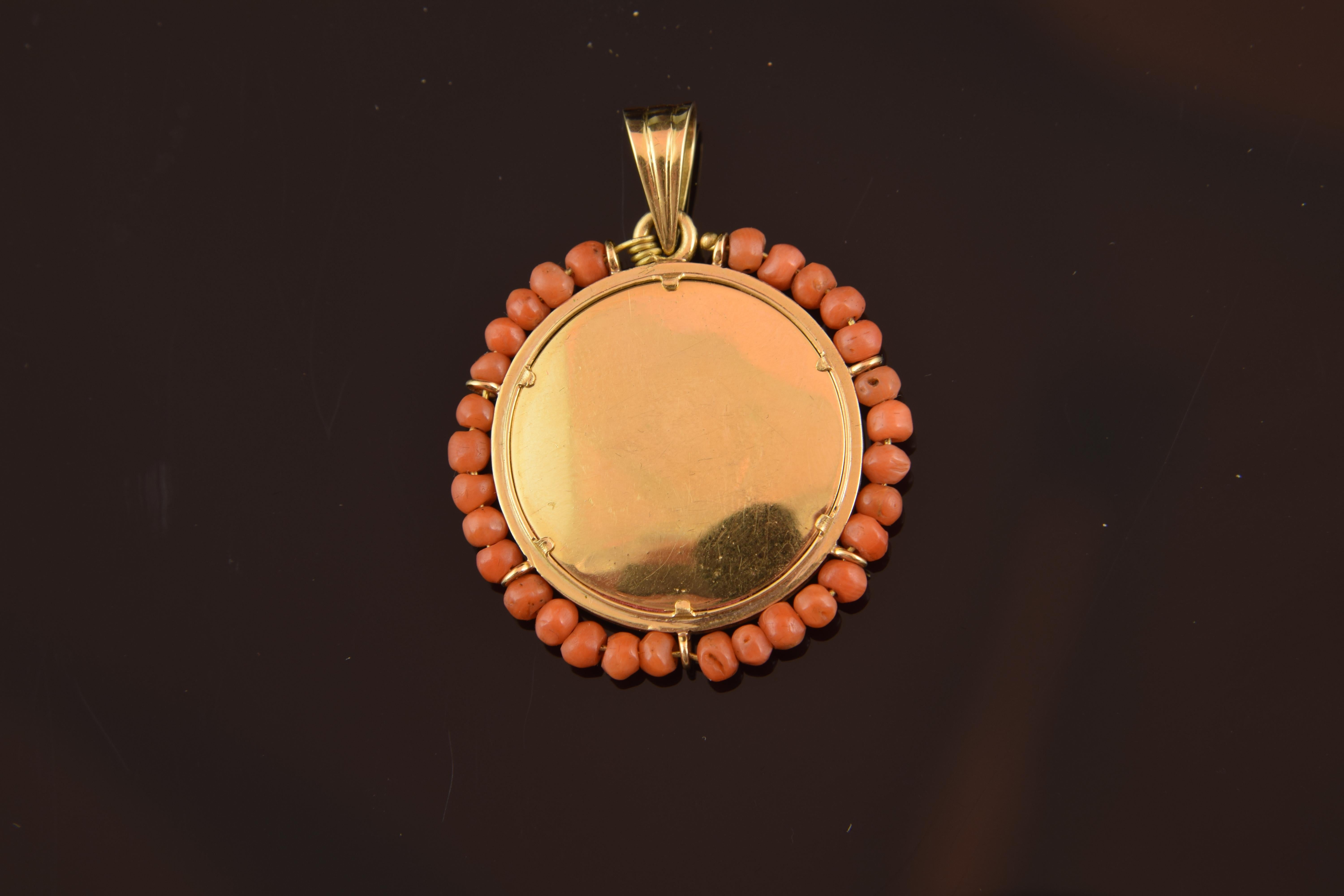 Devotional pendant of enamel on metal that shows, on one side, a bishop with a staff holding a Crucified in his hands, and the other side smooth, with the metal in view. It has been highlighted and decorated with a string of carved coral pearls. It