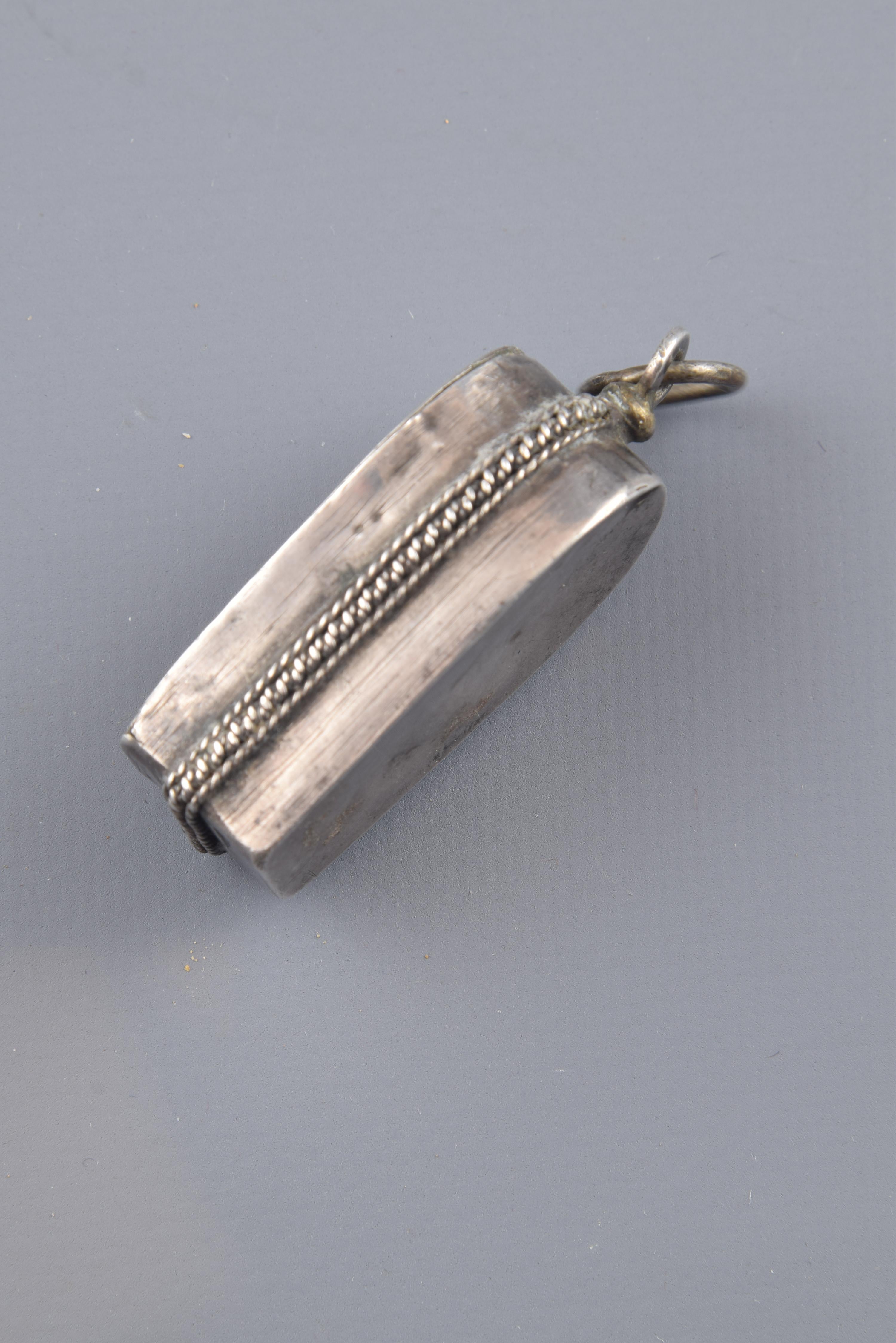 Devotional pendant with rectangular base and topped by semicircular shape decorated to the outside with two thin metal cords flanking another wider and spiral in the same material. While the back has been left smooth, the front, thanks to a
