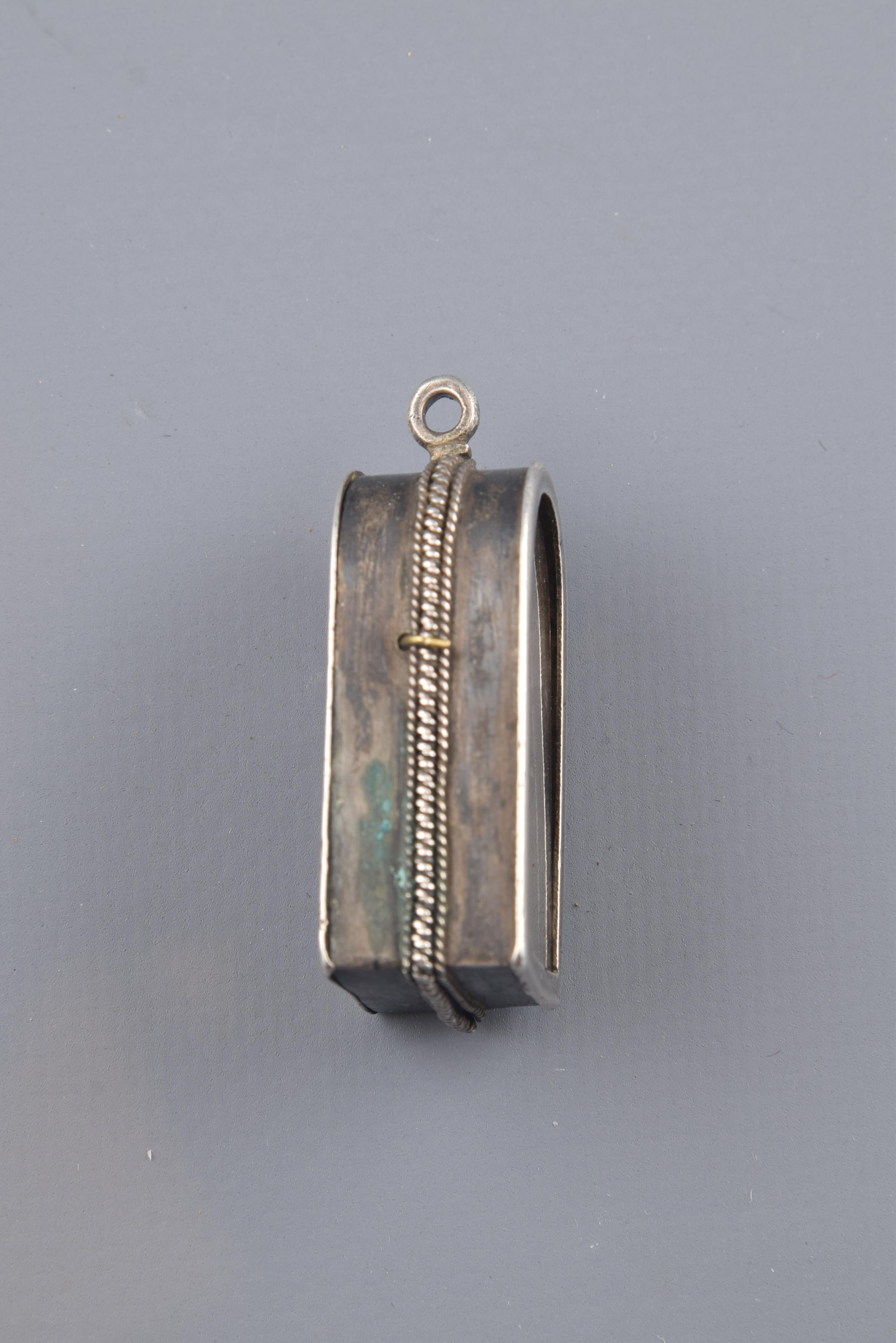 Devotional pendant with rectangular base decorated on the outside with two thin metal cords flanking a wider one in the same material. Both the back and the front have transparent glass sheets that allow to see the polychrome sculpture in the