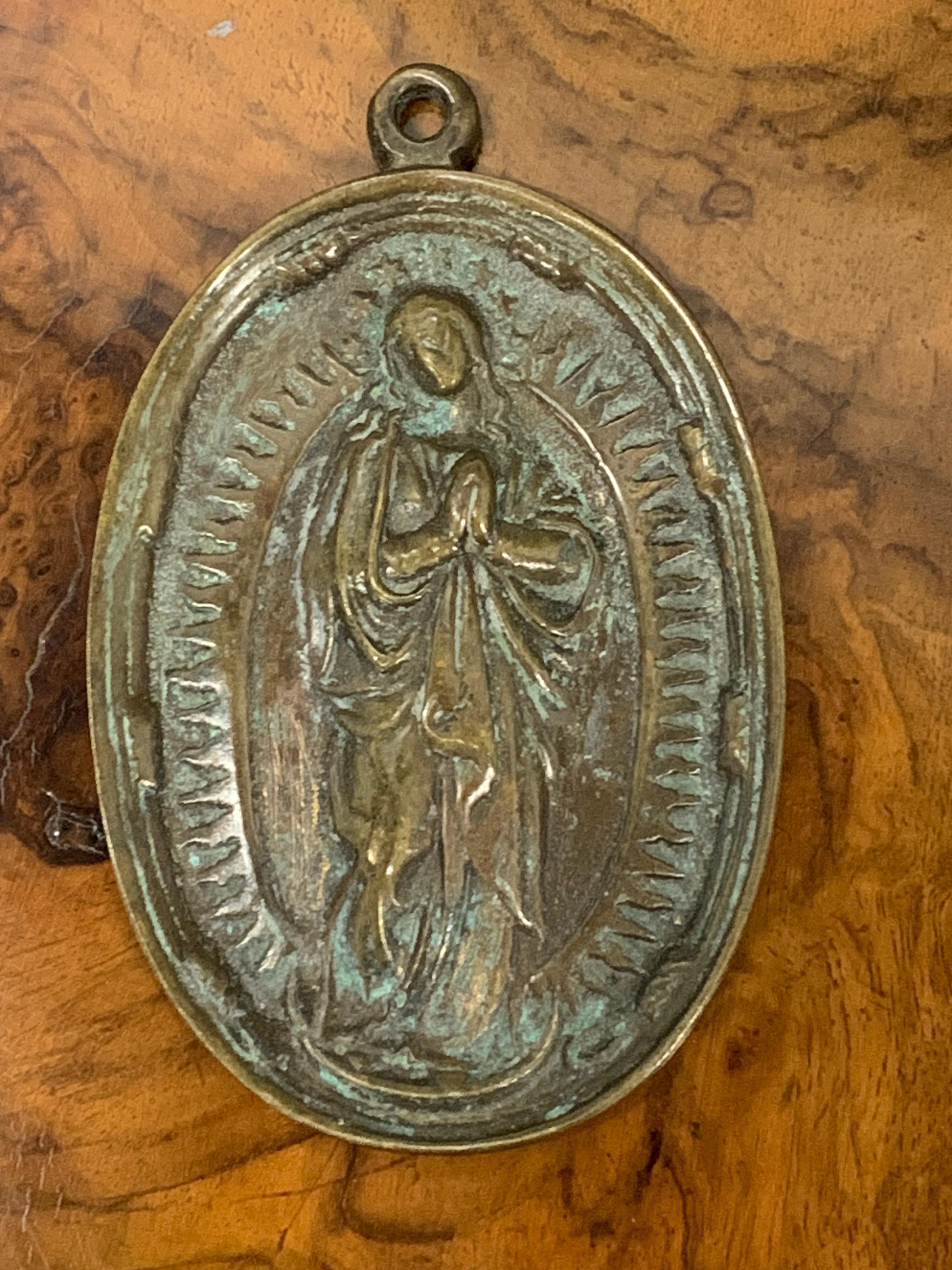 Devotional plaque, Immaculate Conception. Bronze. Spanish school, 17th century. 
Bronze devotional plate with washer at the top that presents a relief on the front. In this you can see the Virgin Mary on a crescent moon, surrounded by light and