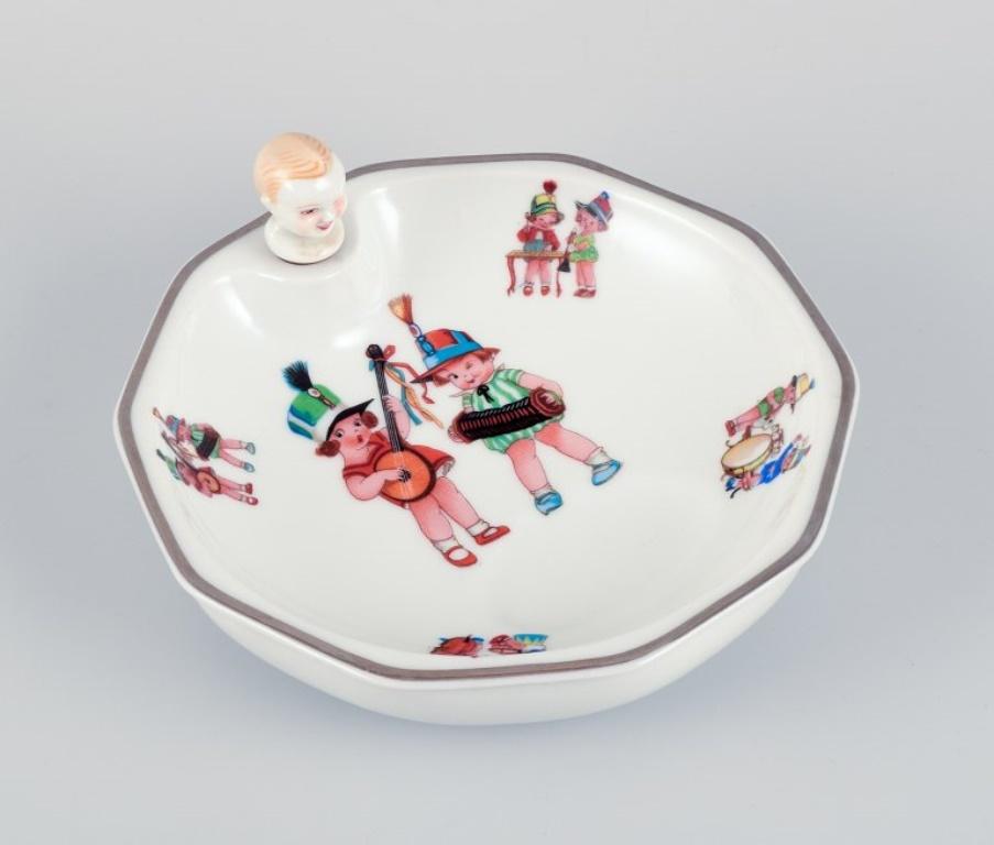 D.F. Limoges, France. 
Porcelain baby warming bowl. Stopper with a child's face. 
Silver rim. Motifs of child musicians.
1930s/40s.
Marked.
Perfect condition.
Dimensions: D 18.0 cm x H 4.5 cm without the stopper.
