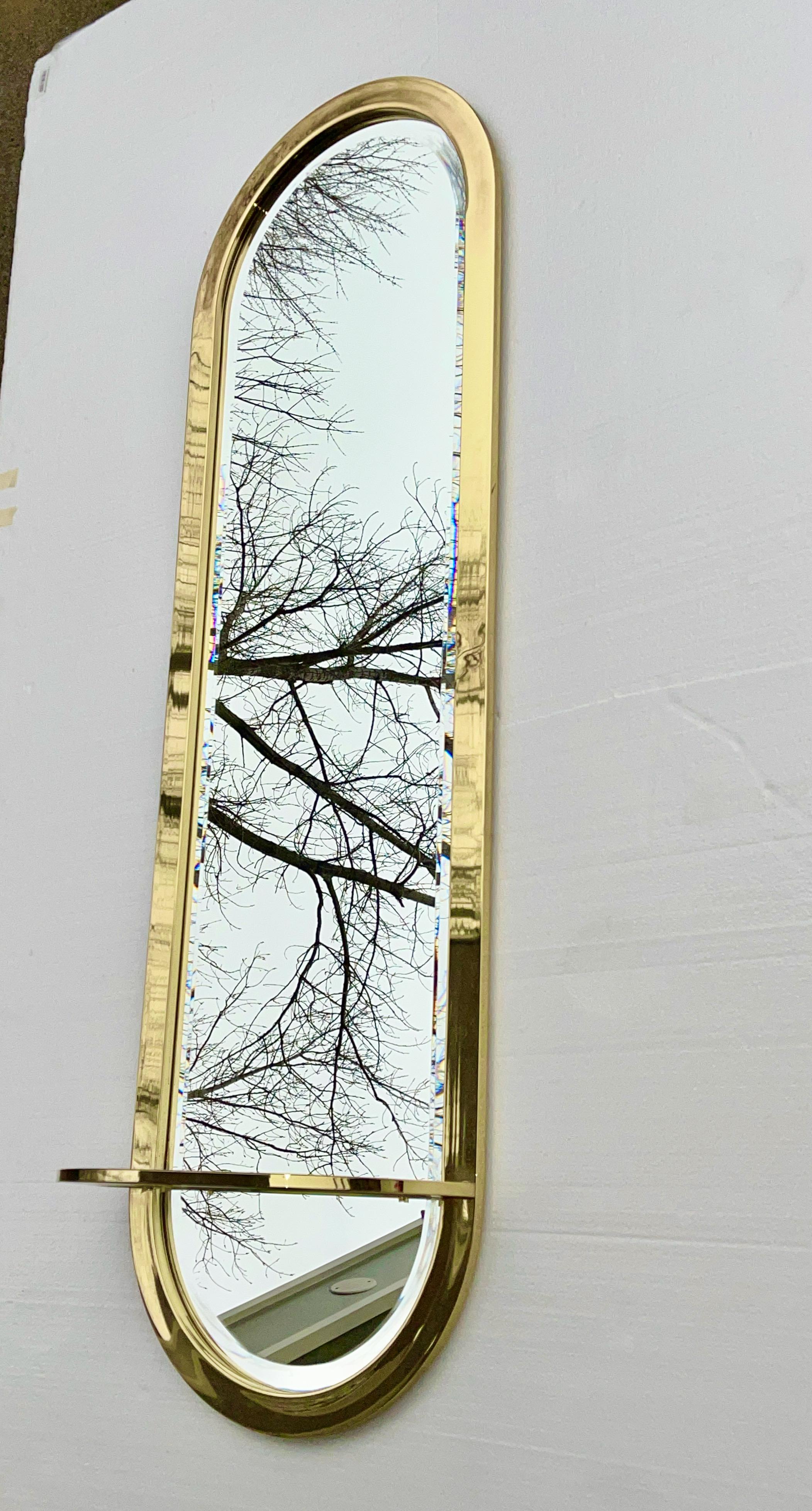 Miroir mural vertical DIA des années 1970 de forme ovale en forme de piste de course avec un encadrement en laiton autour du miroir biseauté et une étagère de console en démilune avec insert en verre trempé transparent.

Voir notre annonce séparée