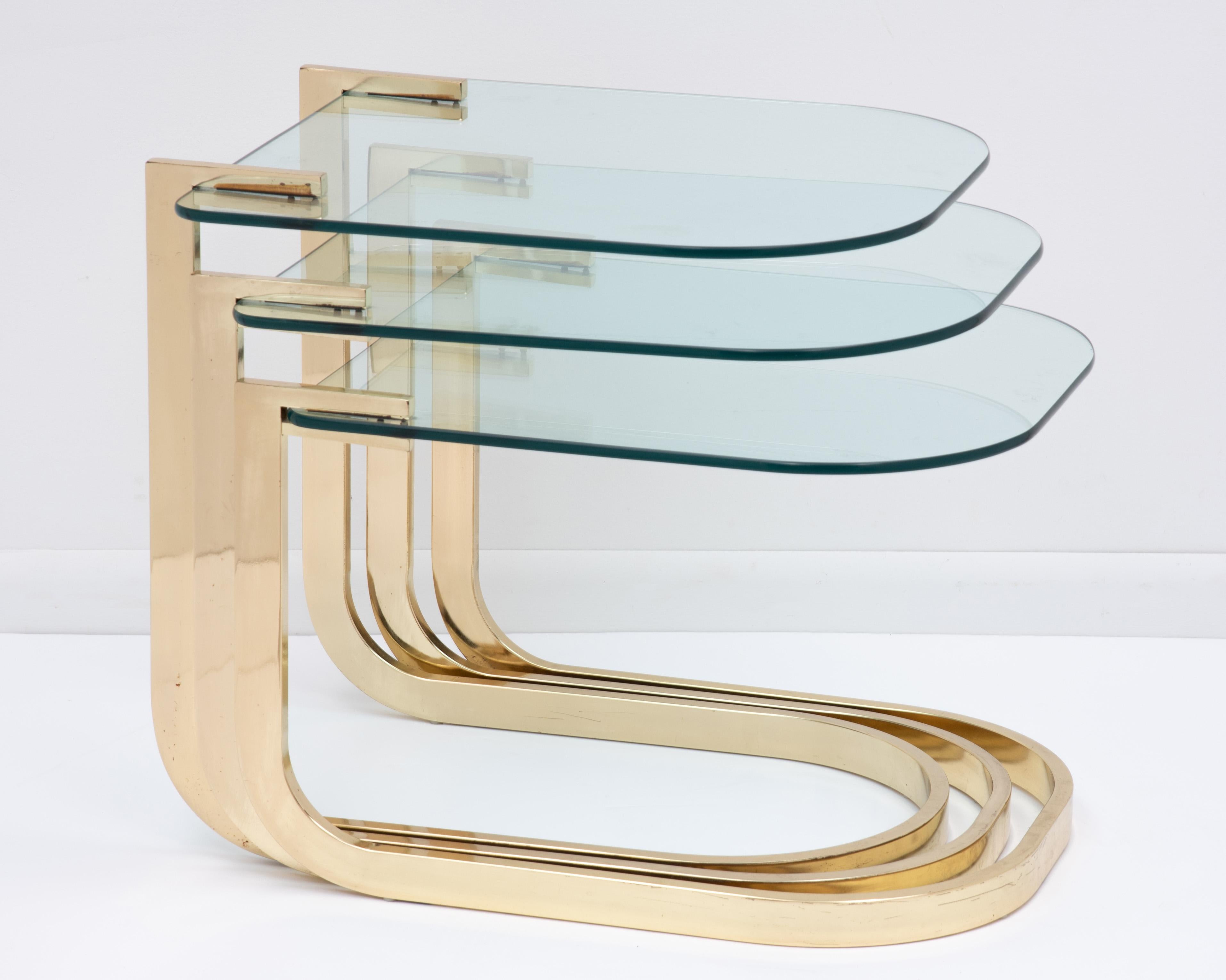 A set of three cantilevered glass and brass nesting tables designed by Milo Baughman for DIA (Design Institute of America). Fully marked with the DIA foil label on the underside of the middle table, ca 1984 serial number 82566. The reflection of the