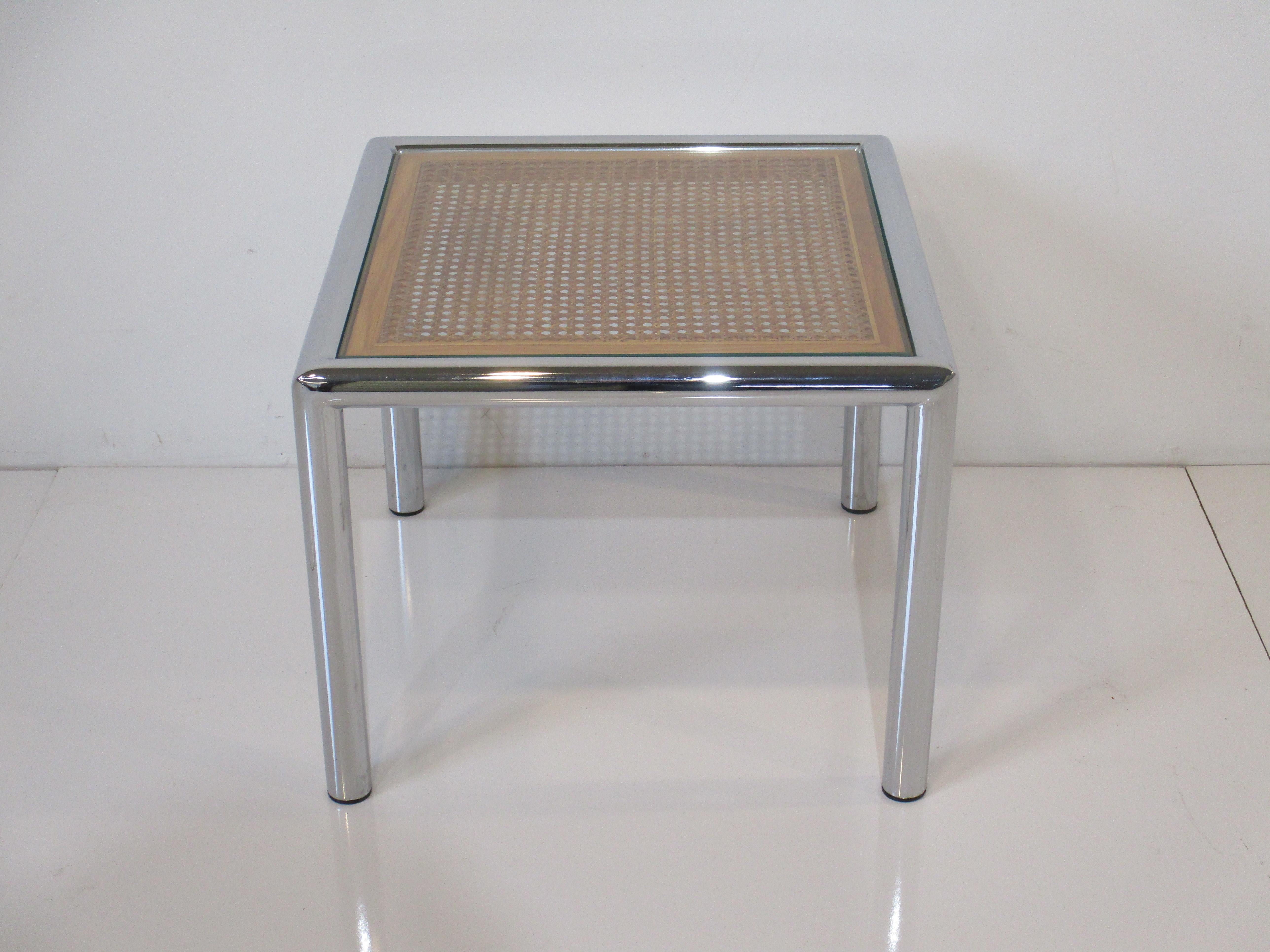 A chrome and woven cane topped side table covered in glass giving the piece a streamline and lighter feel . Strong rounded leg design and the wood frame around the caning shows the care to details in the piece manufactured by DIA Design Institute of