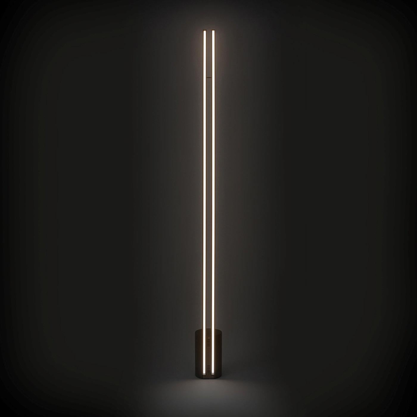 Diese atemberaubende Stehlampe ist der Inbegriff von moderner Eleganz und minimalistischem Flair. Die Metallstruktur mit bronzefarbenem Finish besteht aus einem zylindrischen Sockel, aus dem zwei parallele, stromlinienförmige Segmente herausragen,