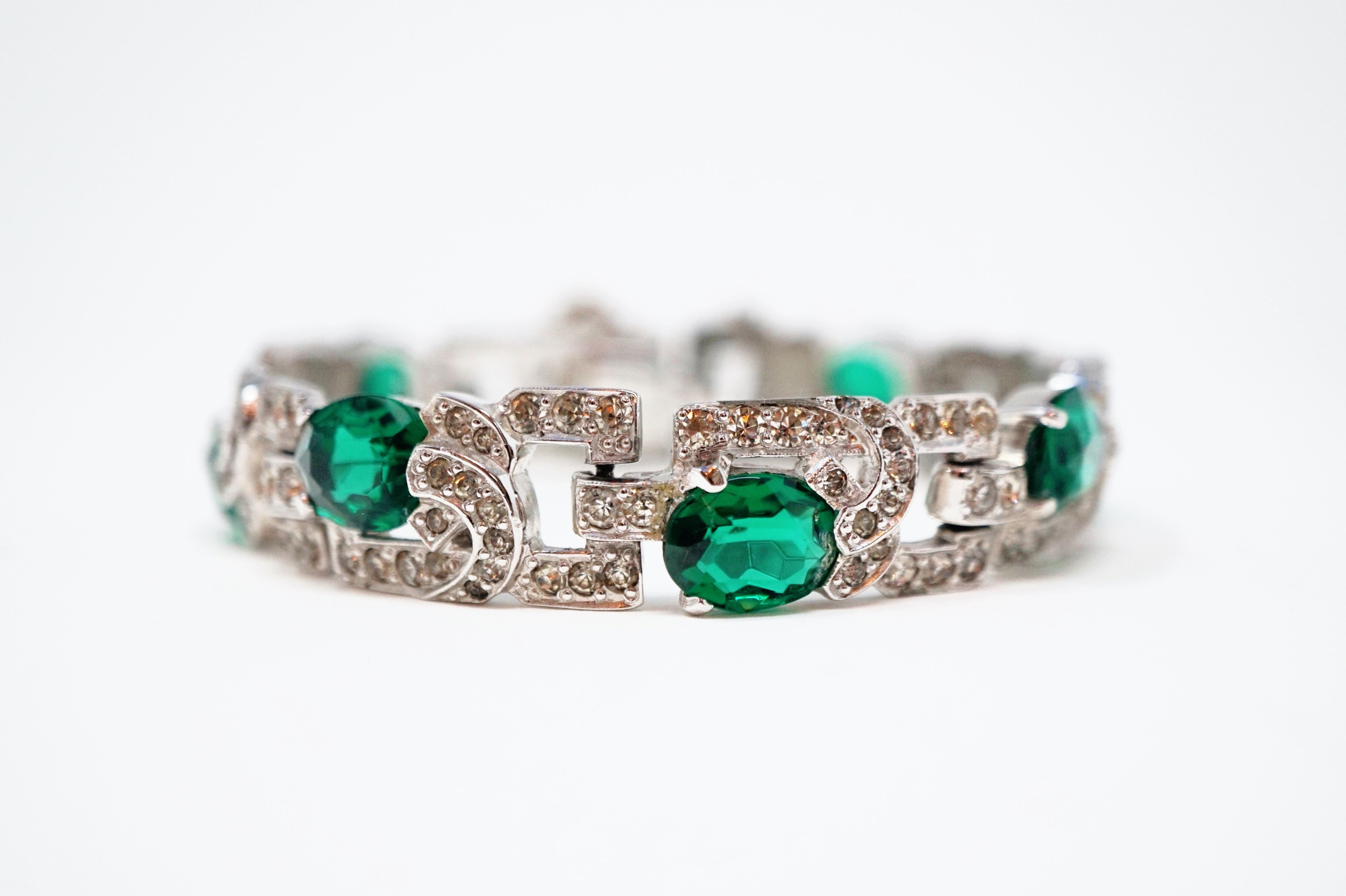 This absolutely breathtaking piece by Mazer Brothers, circa 1940s, is a true treasure from the past!  A classic art deco tennis bracelet is covered in shiny rhodium plate, studded with Diamanté crystals, and accented with oval Emerald-colored