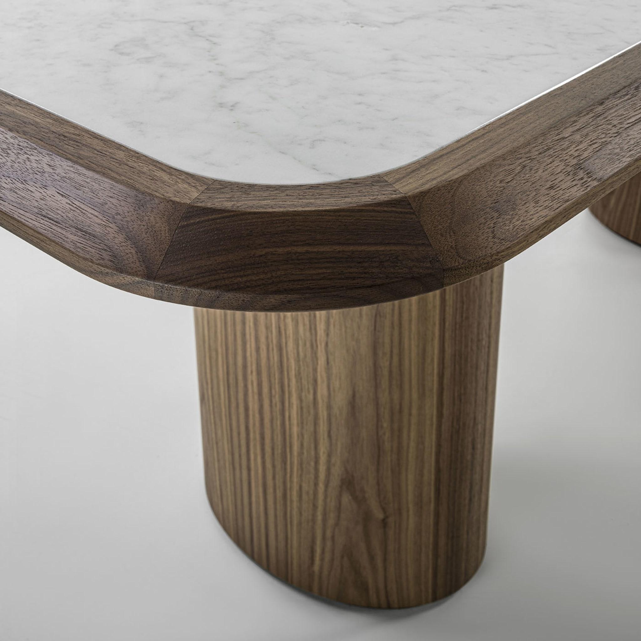 Sophisticated details refusing sharp angularities perfect the already harmonious silhouette of this dining table, crafted of prized Canaletto walnut. Sustained by a couple of column-like legs, the stunning Carrara marble top is set in a refined