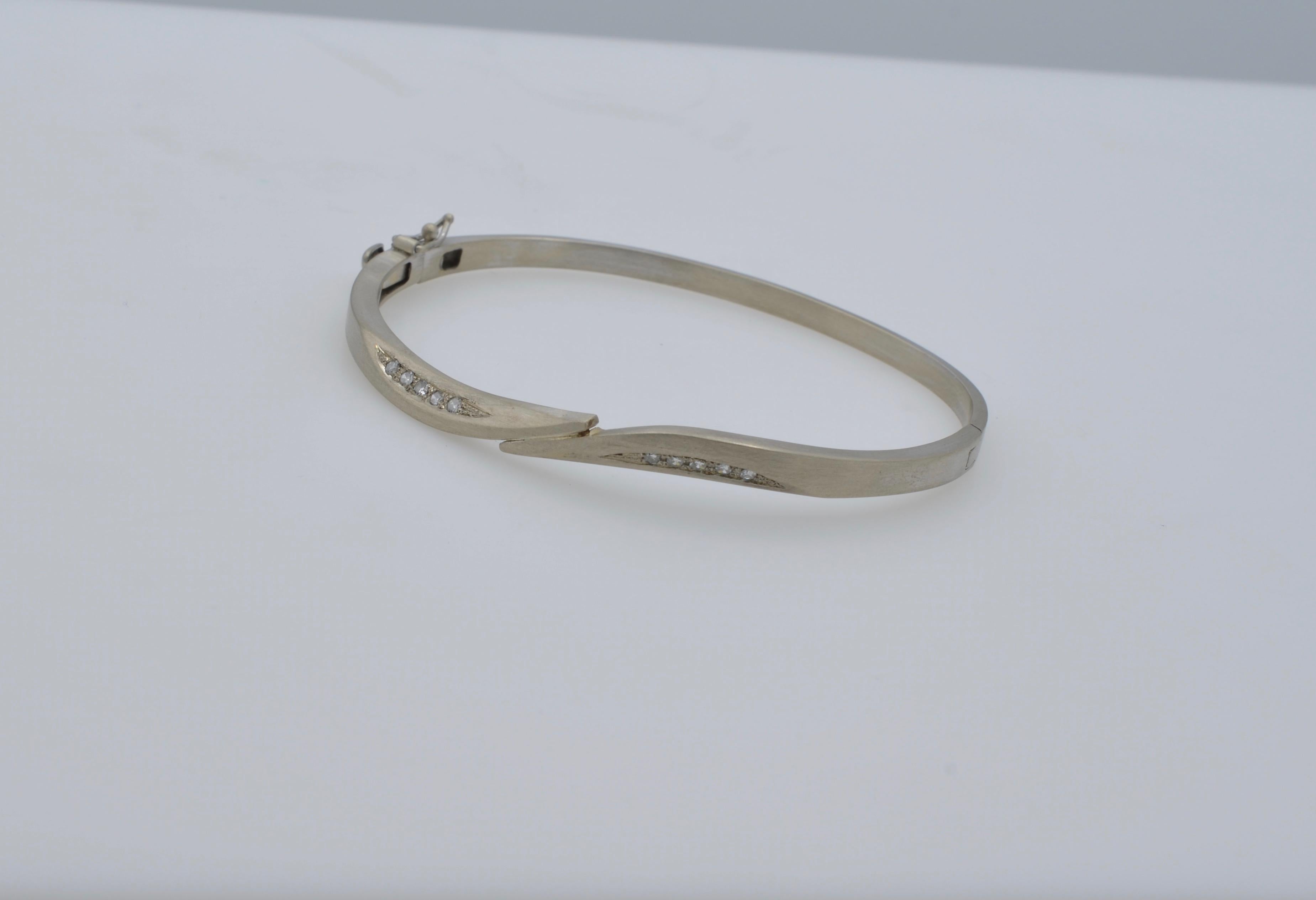 This white gold and diamond bangle is modern, sleek and sexy! The 'kissing' on the center frames the five diamonds ( aprox 0.20 tw ) beautifully set in a 'wave' on each side. It is a lovely design that is timeless and special. The closure has a very