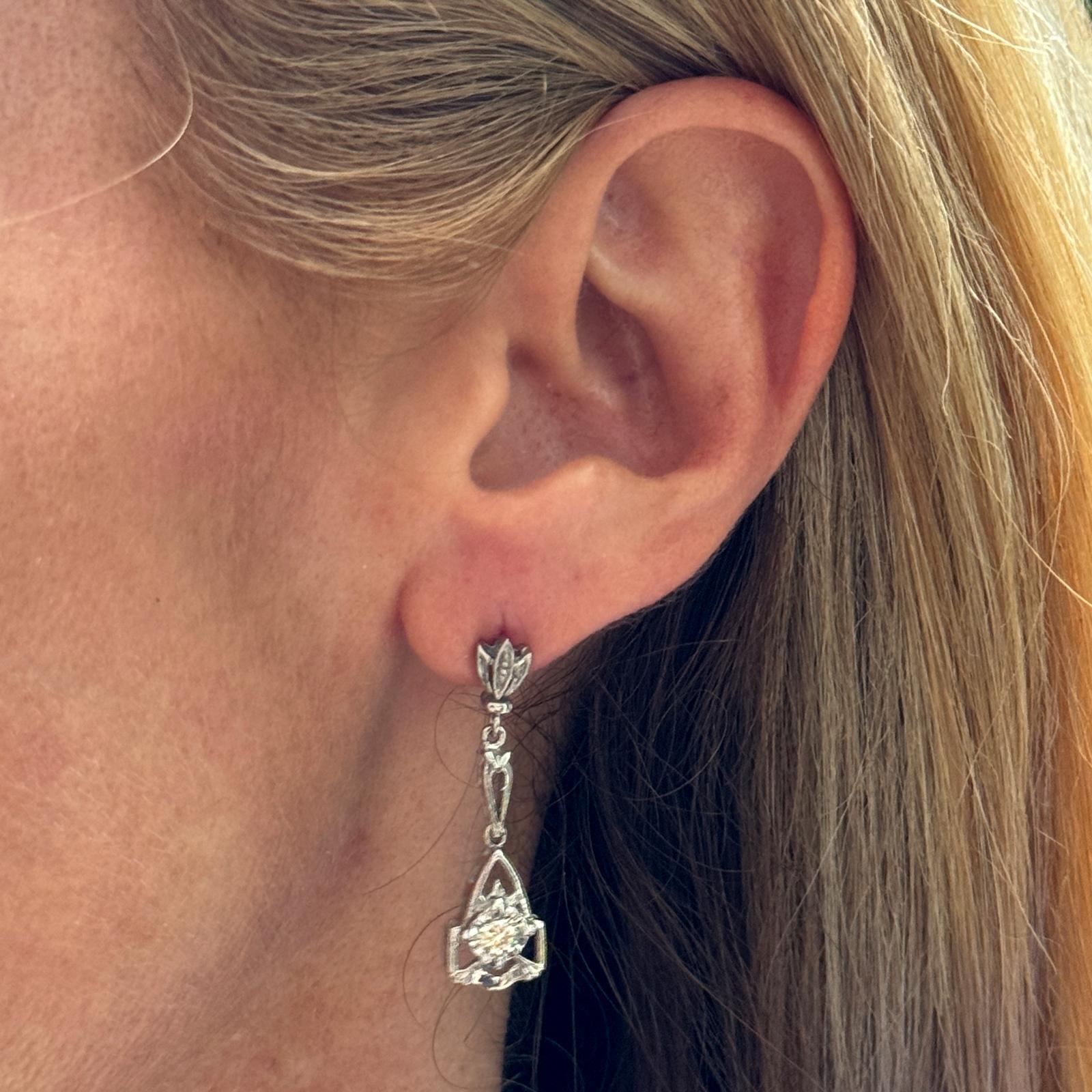 Modern Diamond Dangle Earrings feature a minimalist design, each earring showcasing a single round brilliant-cut diamond set in 14K white gold. The diamonds weigh approximately .40 CTW and are suspended from a sleek, modern dangle setting, allowing