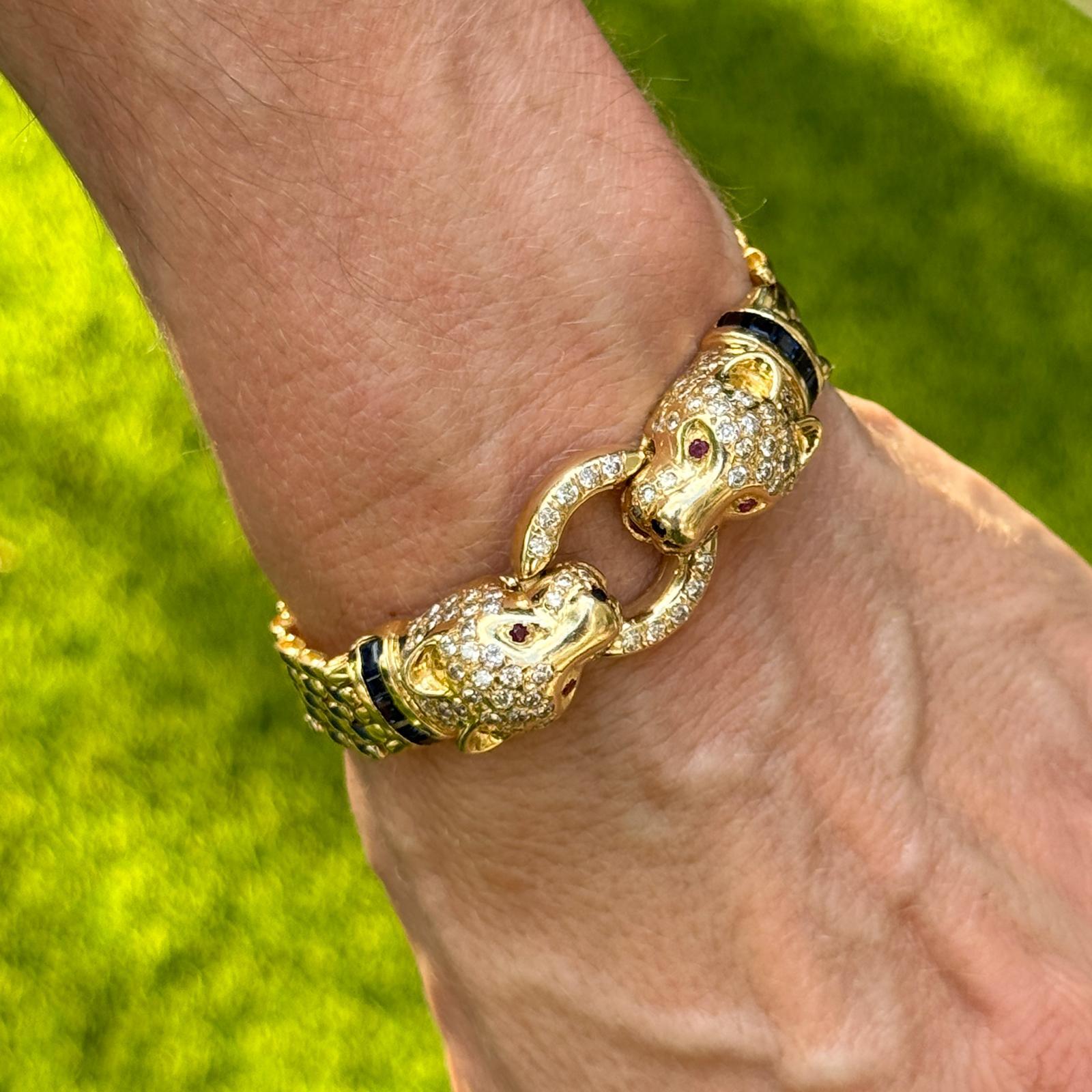 This exquisite 14 karat yellow gold Diamond, Sapphire, and Ruby Panther Bracelet features a bold and luxurious design, with 104 round brilliant cut diamonds totaling approximately 3.00 carats (H-I color, SI clarity) set along the bracelet. The two