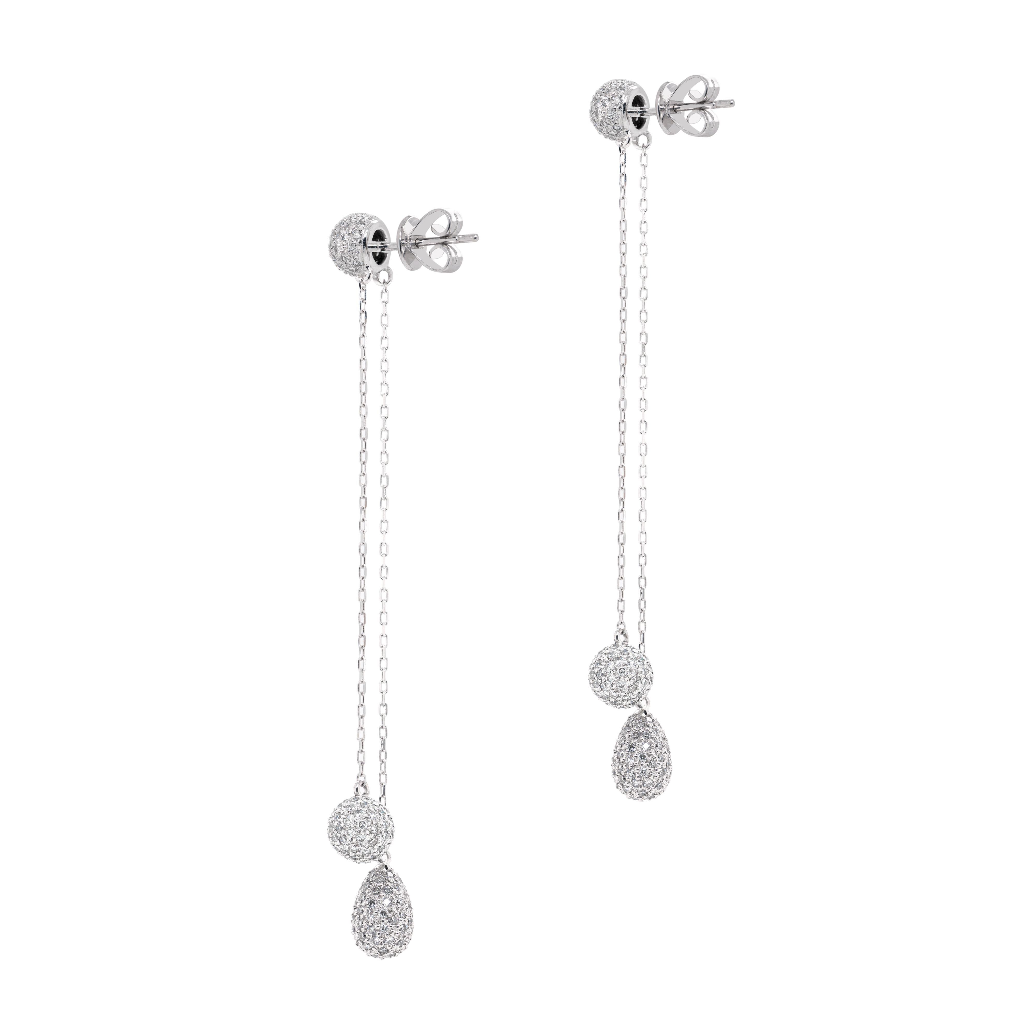 These 18 carat white gold drop earrings are beautifully designed with two asymmetric delicate chains, one ending with a ball inlaid with fine round brilliant cut diamonds and the other ending with a drop, also inlaid with fine round brilliant cut