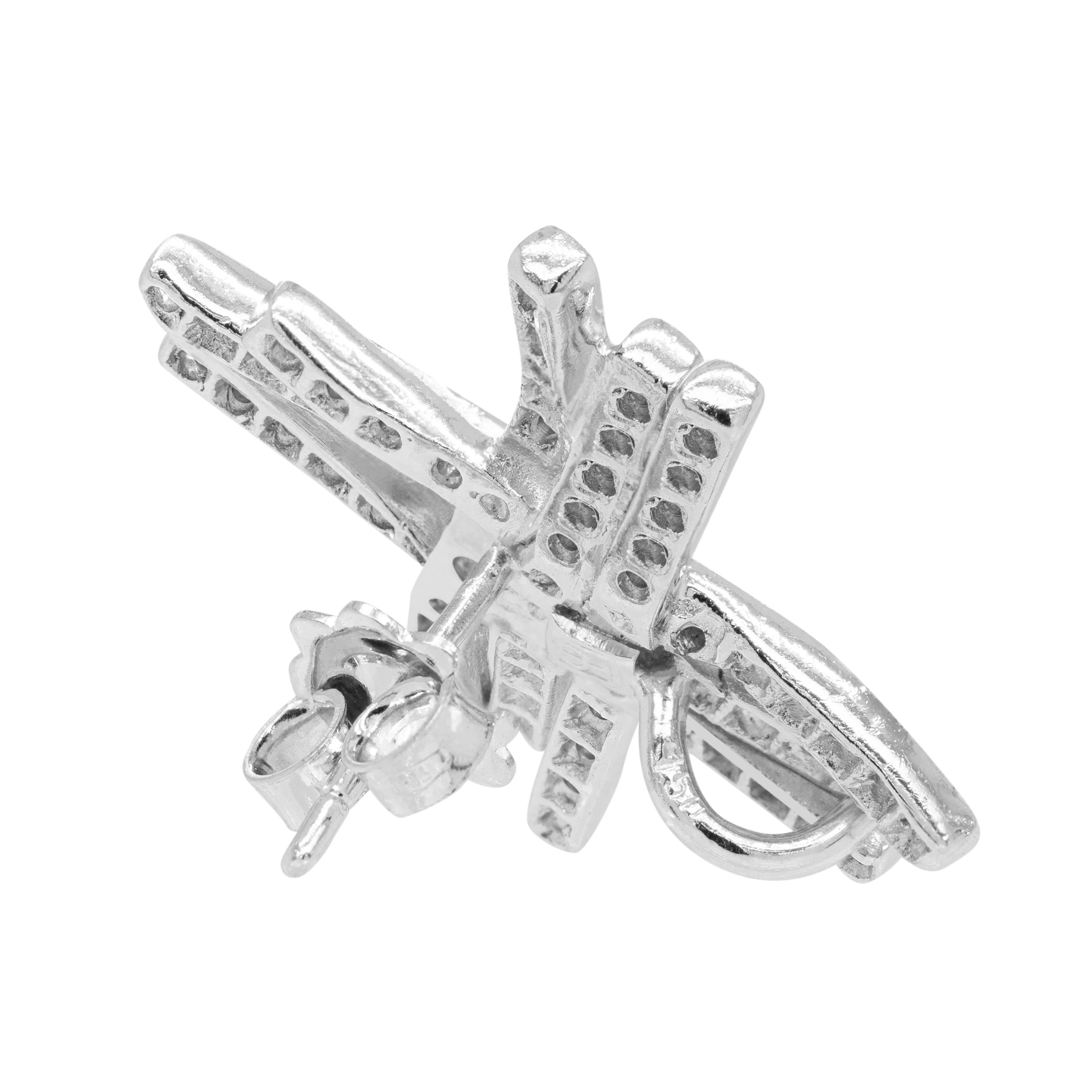 These beautiful 18 carat white gold stud earrings feature an abstract design, composed of six thin asymmetrical ribbons grouped into sets of three and braided together in the middle to create overlapping cross motifs. 

The delicate ribbons are
