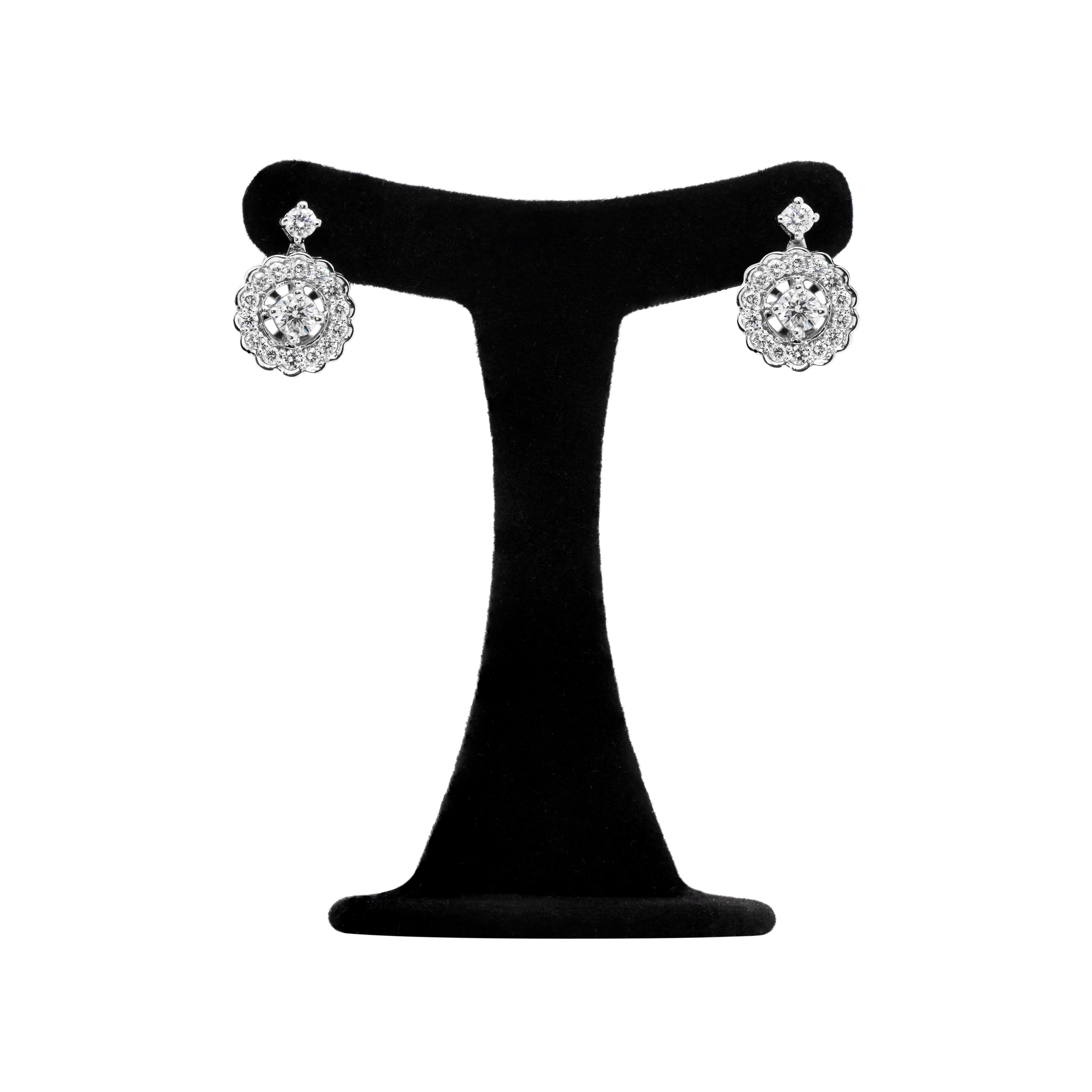 These diamond cluster drop earrings feature a round brilliant cut diamond claw set in the center beautifully surrounded by a further 14 round brilliant cut diamonds in a rubover scalloped mount. The cluster hangs from a single stone diamond stud,