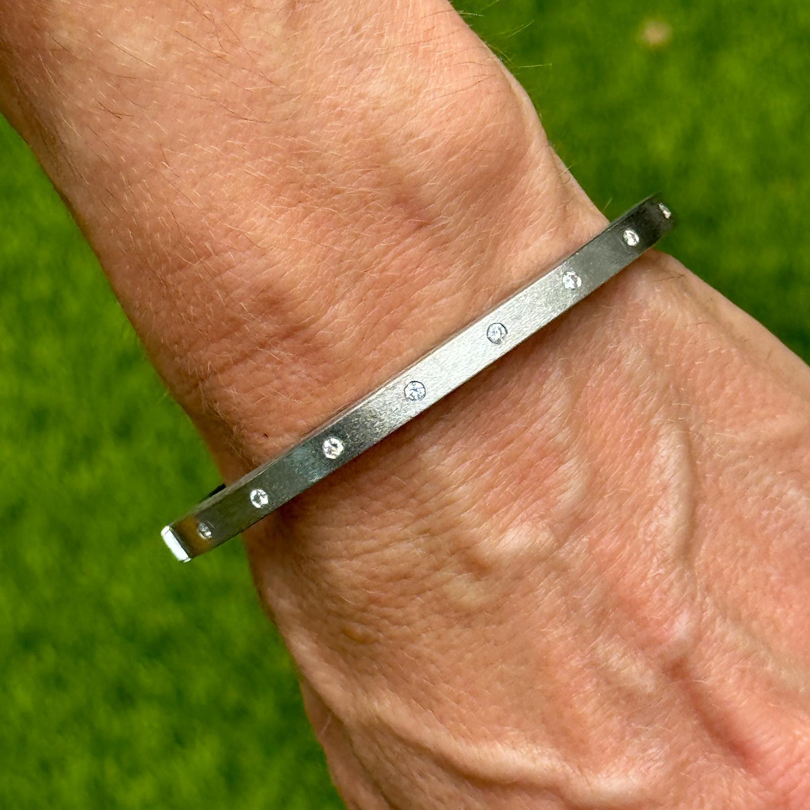 This modern hinged bangle bracelet is crafted from 18 karat white gold with a satin finish, featuring a sleek squared-off design. Accented by 8 round brilliant sparkling diamonds, the bracelet offers a refined blend of contemporary style and