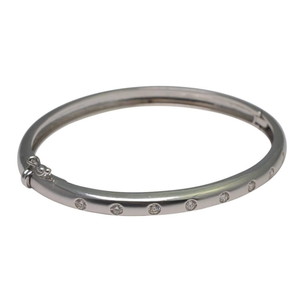 Contemporary diamond half hoop bangle in 18ct white gold; the bangle is inset with 9 brilliant cut diamonds totalling 0.55ct in brushed gold with the underside in polished gold.  It opens on a side hinge and and is fitted with a figure-of-eight