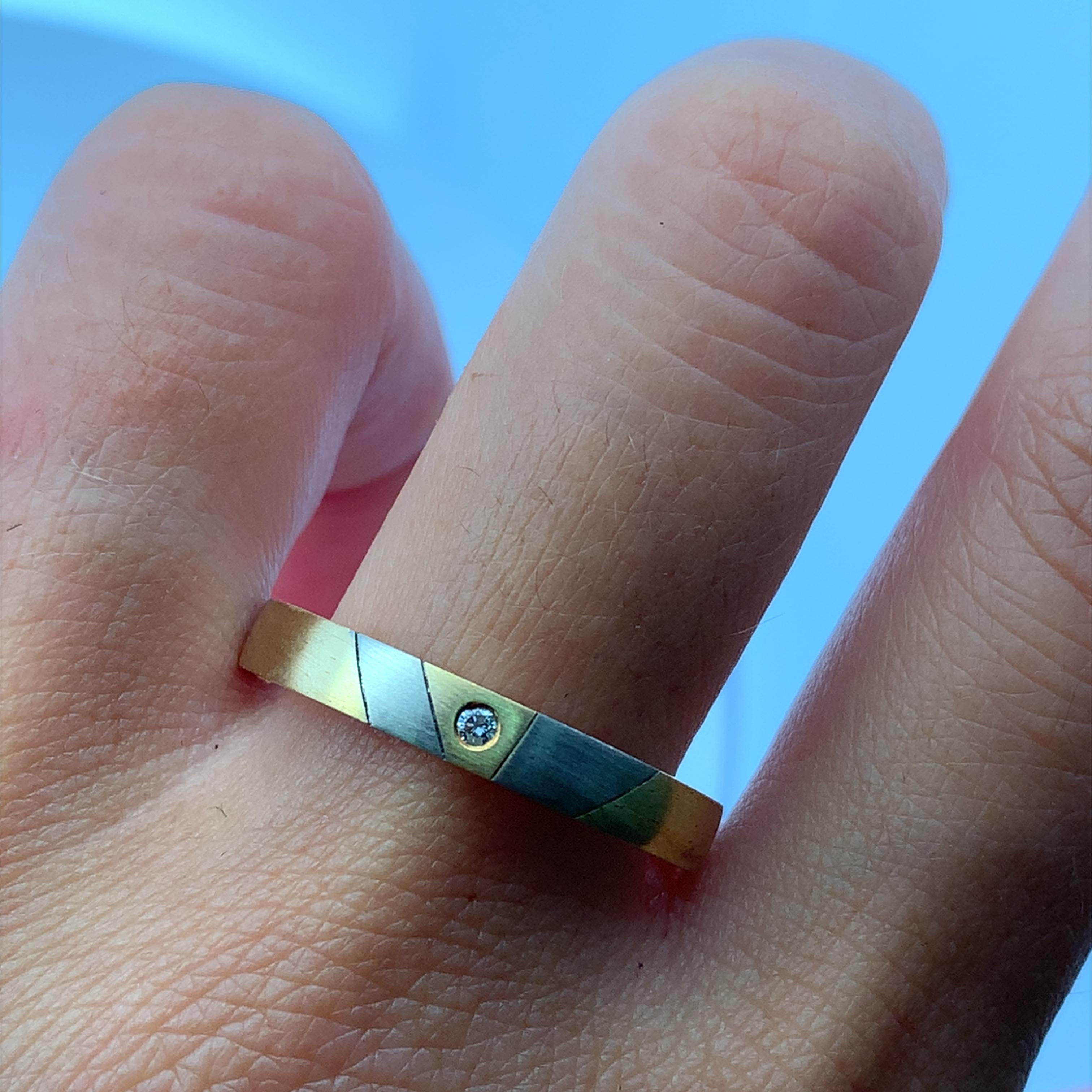 Erhöhen Sie Ihren Stil mit diesem modernen Unisex-Ehering aus 18 Karat Gelb- und Weißgold mit matter Oberfläche, der fachmännisch aus strahlendem 18 Karat Gelbgold gefertigt ist. Mit kontrastierenden Intarsien und einem runden Diamanten im