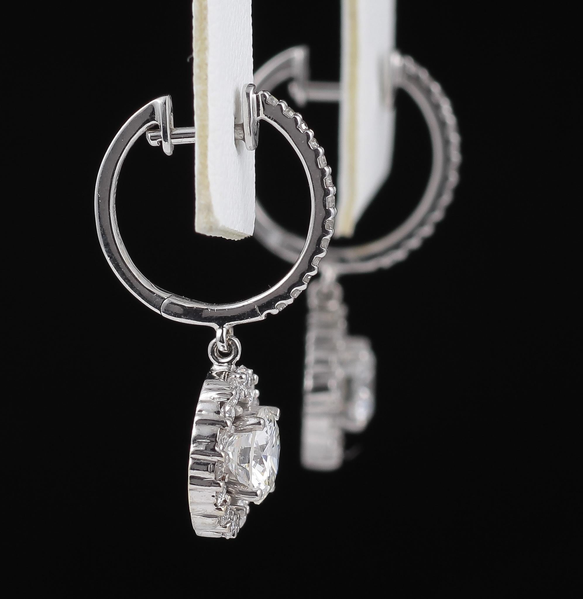 These are a stunning pair of  Diamond Halo Dangling Earrings fabricated in 14 Karat White Gold. These earrings feature a prong set Round Brilliant Cut Diamond, approximately 0.70 Carat at the center of a halo of  sparkling diamonds. The Diamonds are