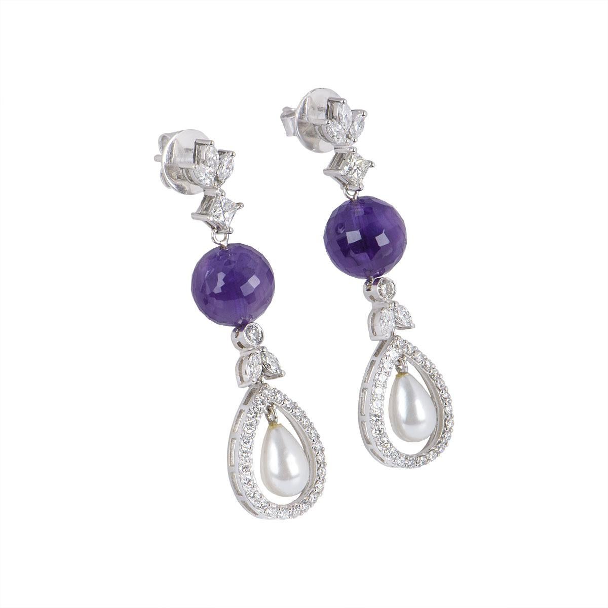 A pair of 18k white gold diamond and multi-stone earrings. The earrings feature 3 marquise cut diamonds with a princess cut diamond below it followed by an amethyst shaped ball with a pearl freely moving at the bottom, surrounded by openwork pave