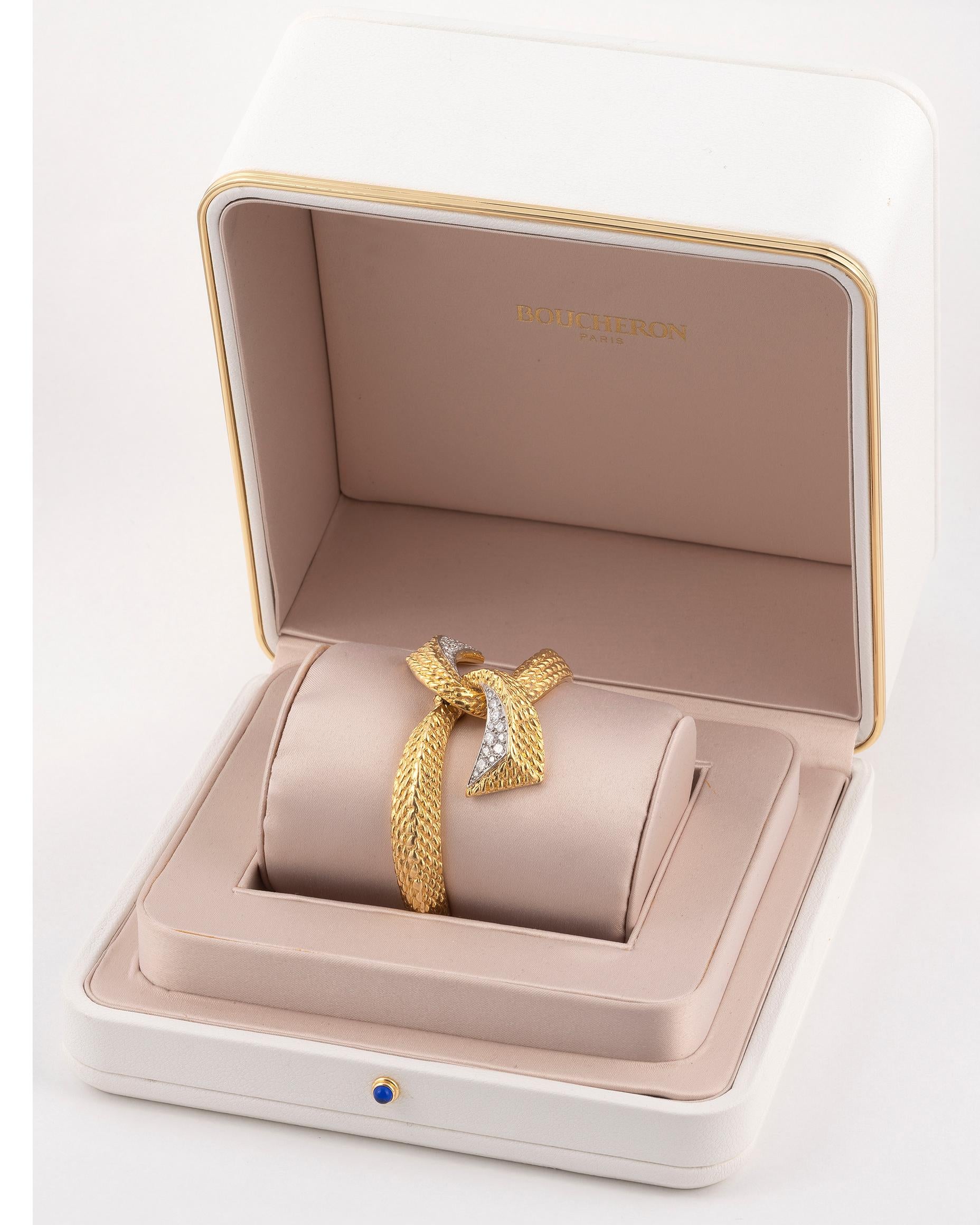 The rigid opening bracelet in textured 18K yellow gold topped with a large knot paved with brilliant-cut diamonds in a grain-set setting. 
Signed BOUCHERON and numbered. Gross weight : 72,24 gr. Wrist diameter : 17 cm. In its case.