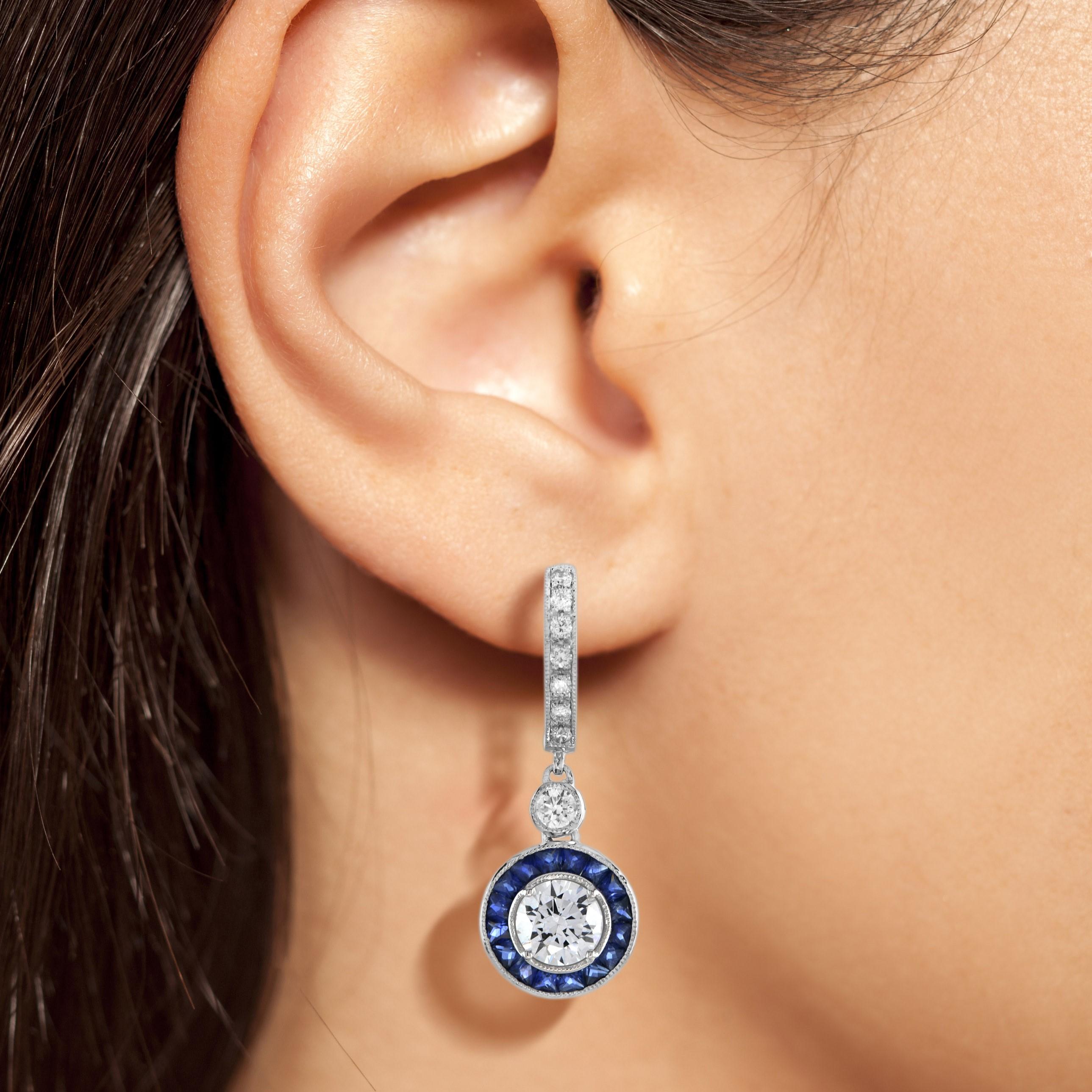 Exquisite, vom frühen Art déco inspirierte Ohrringe mit Diamanten und blauem Saphir. Der zentrale Diamant ist von fein gefassten, doppelten Saphiren umgeben, die eine schicke achteckige Form bilden. Die Ohrringe können perfekt mit dem Halo-Ring im