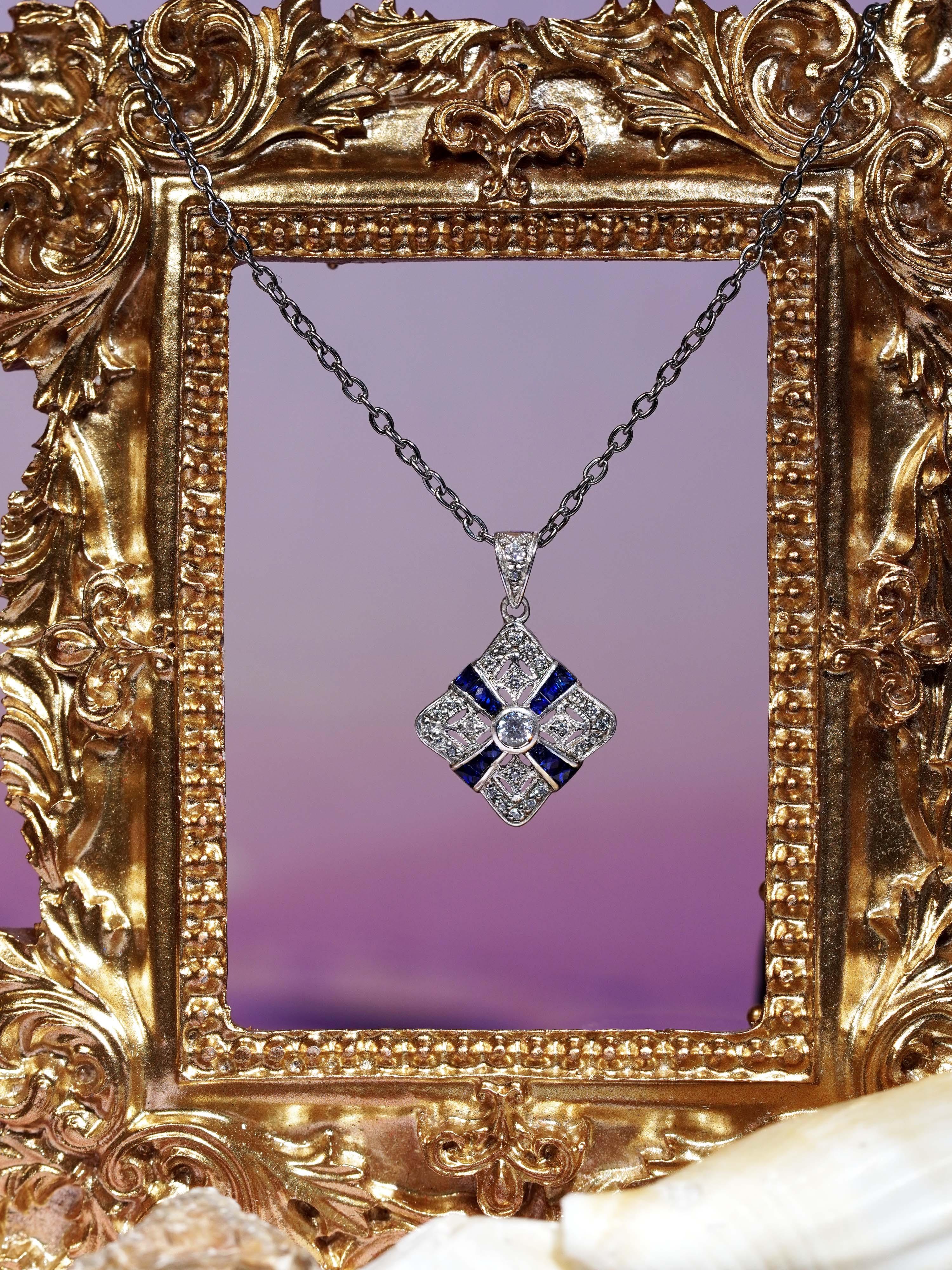 Inspiré par la symétrie gracieuse du design Art déco, ce pendentif présente en son centre un diamant rond serti en chaton, qui rayonne d'une brillance intemporelle. Autour du diamant, des saphirs bleus taillés à la française et méticuleusement