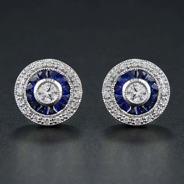Un brillante diamante rotondo al centro, circondato prima da profondi zaffiri blu e poi da una scintillante aureola esterna di diamanti. Il design a strati crea un look audace ma elegante, che riflette la bellezza geometrica dell'epoca Art Deco.