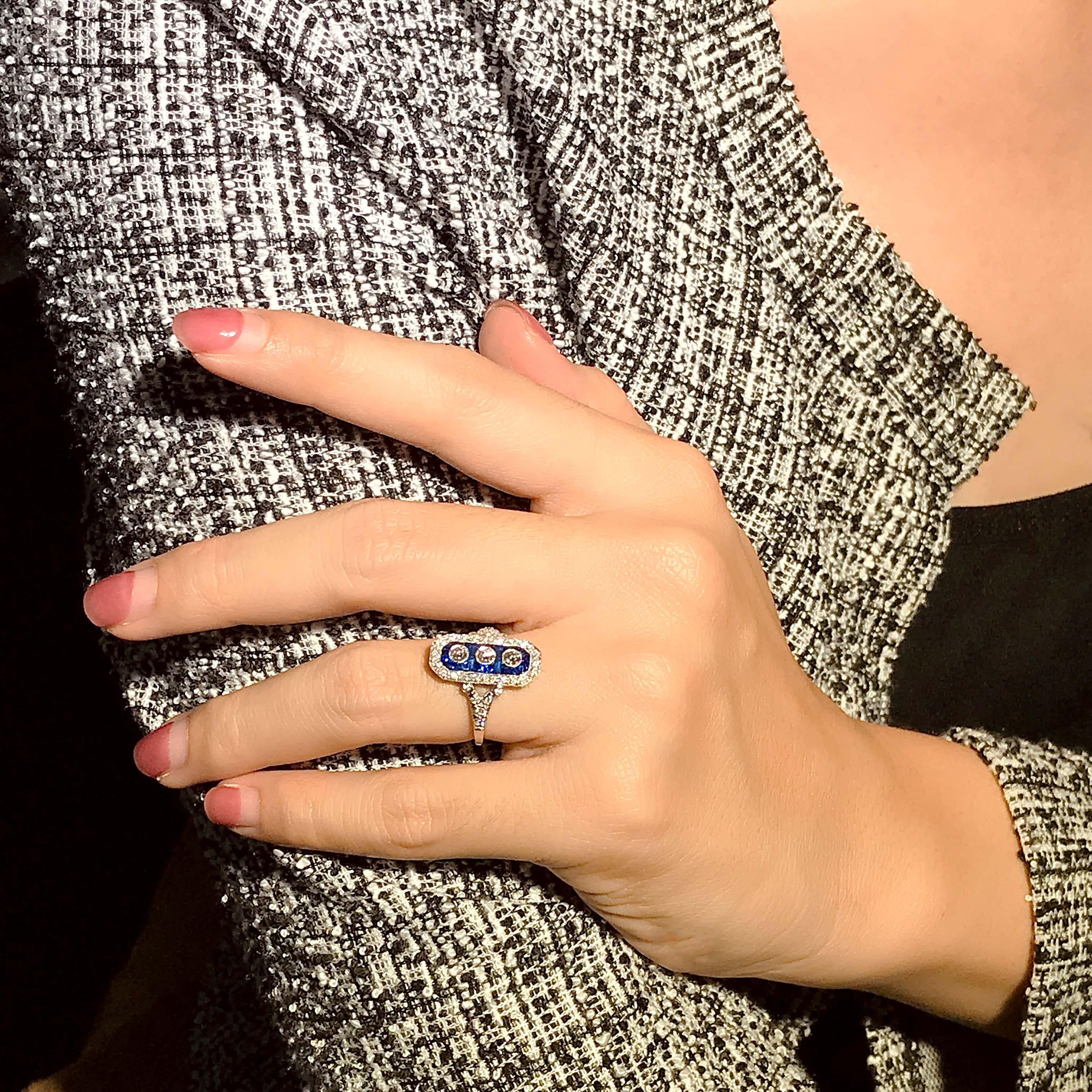 Trois diamants centraux de taille ronde créent un flash d'étincelles vertical et homogène dans cette superbe et impressionnante bague de style Art déco. Le trio scintillant est délimité par une monture octogonale en saphir bleu et diamant qui mène à
