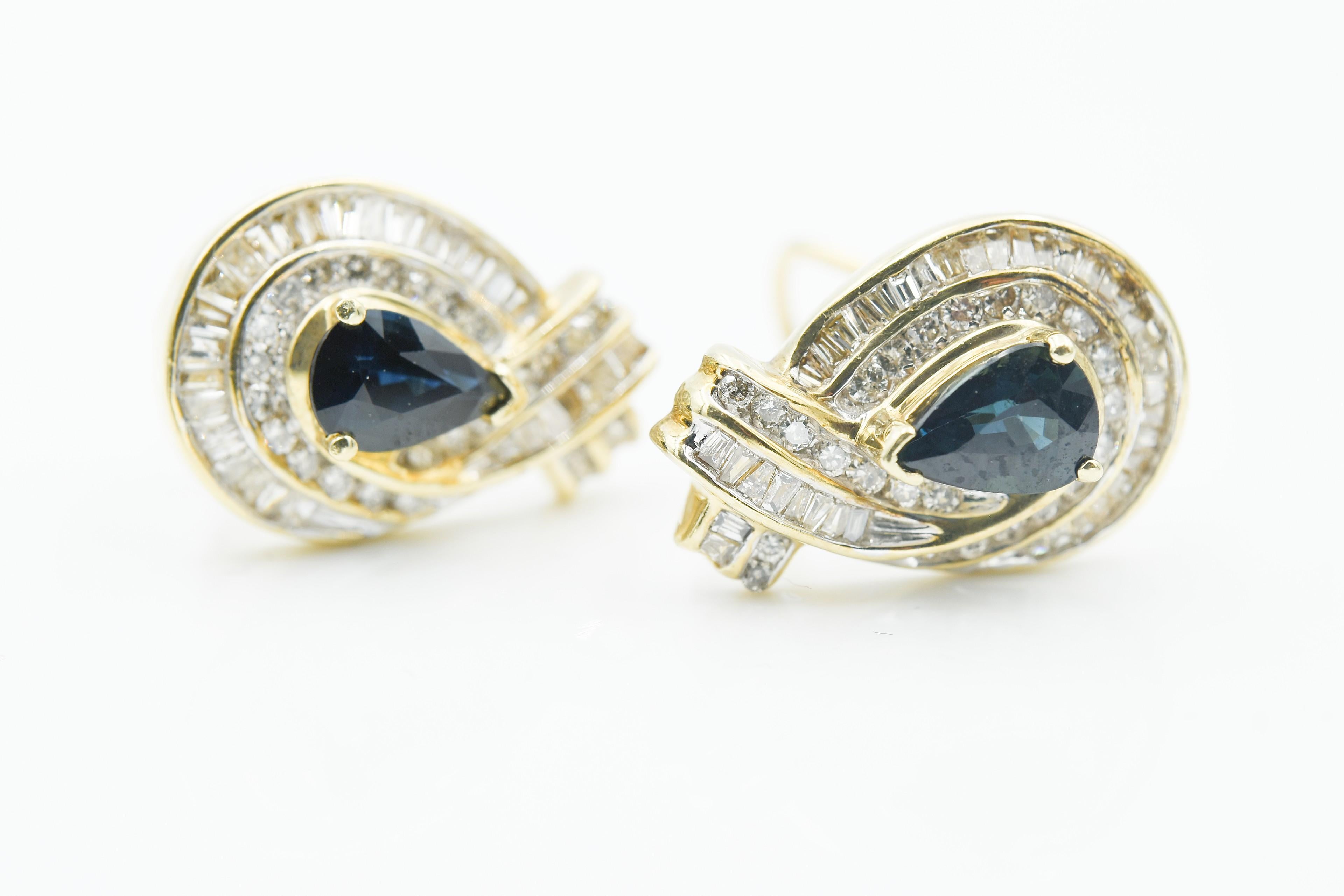 Diamond Baguette and Blue Sapphire Earrings with one carat pear shape Sapphire center stones. Round and Baggett channel set diamonds. 14K yellow gold with omega backs. 6.2 grams 14k gold. Diamond weight 2.2ct total.  Sapphires are medium to dark