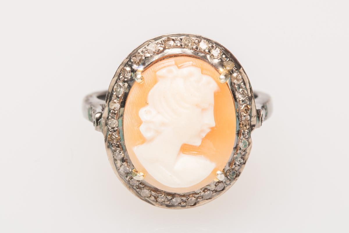 A lovely modern cameo ring set in sterling silver.  The hand-carved shell depicts the profile of a woman with intricate detail facing to the right with a nice translucence when held up to the light.  It is bordered with round, brilliant cut diamonds