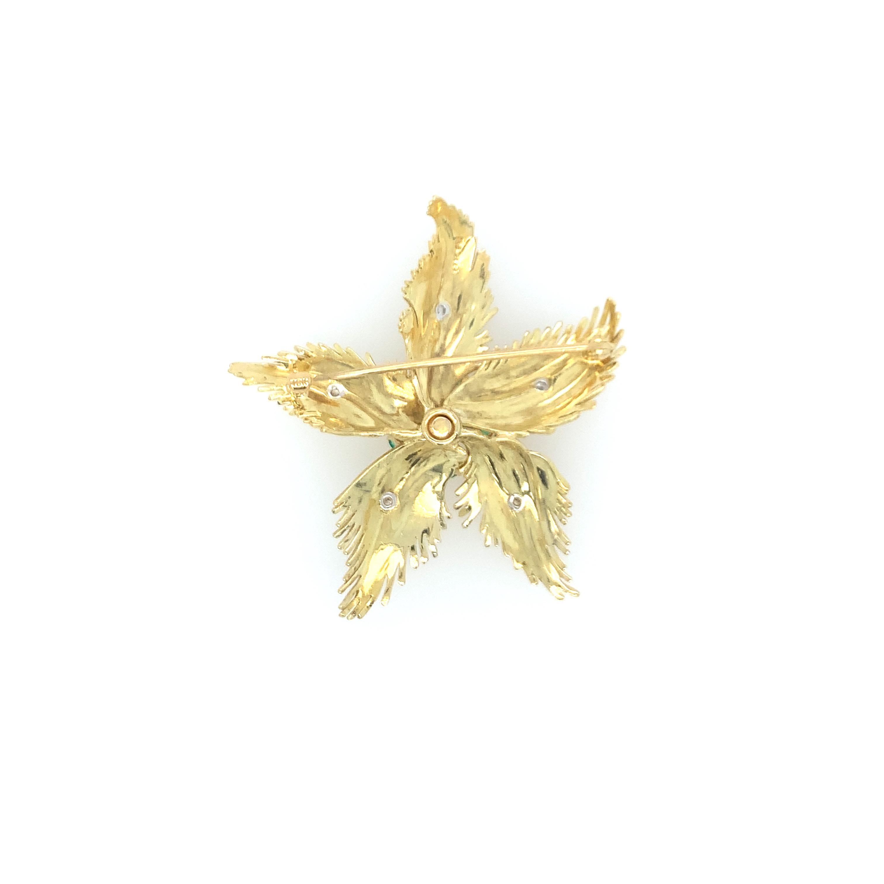 A treasured 18K yellow gold intricate floral brooch featuring (5) feathered gold petals, each highlighted by a single cut diamond. At the center of the floral pin sits a single round diamond surrounded by (5) five emeralds weighing approximately .30