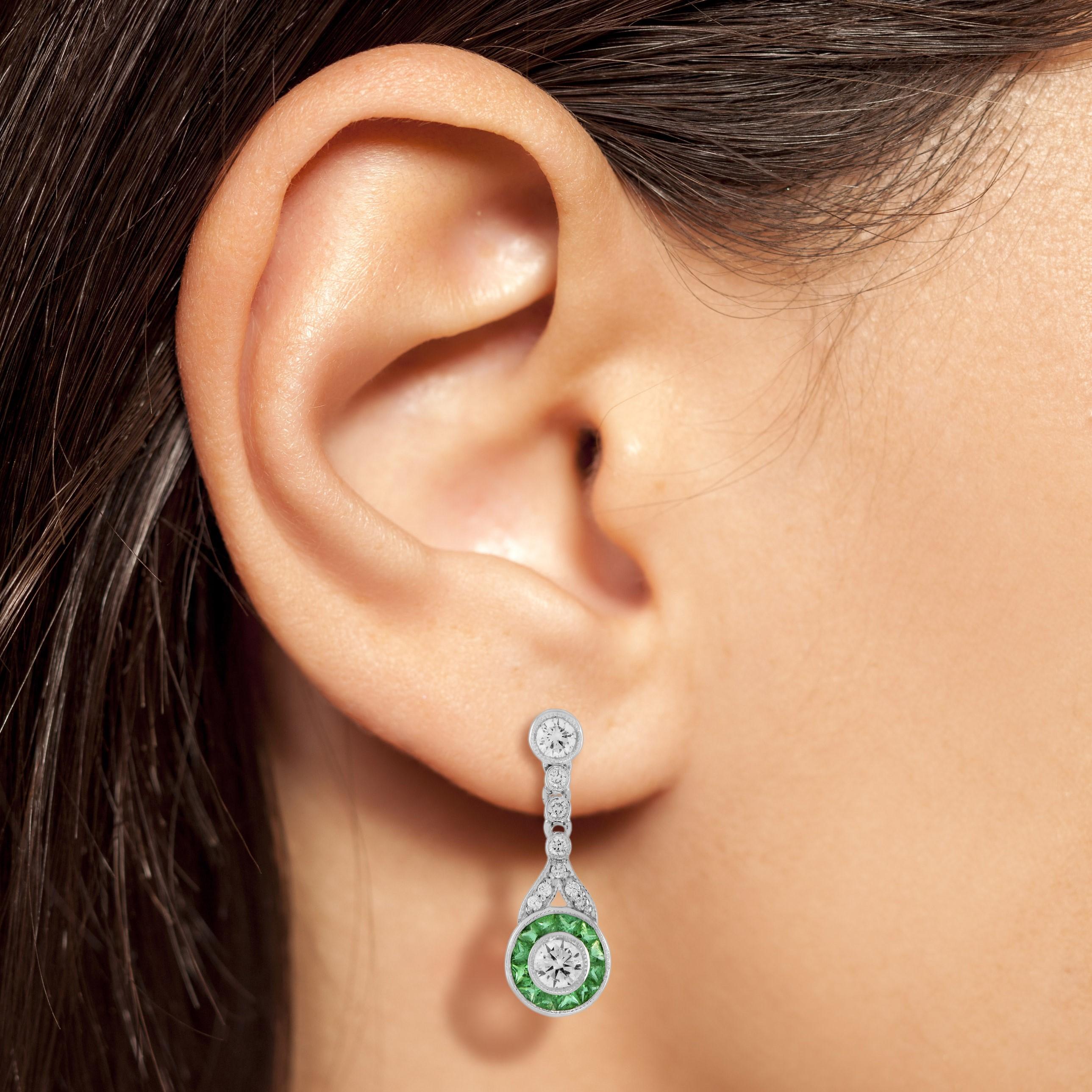 A beautiful pair of white gold earrings that are made with Art Deco era inspiration. They are set with diamond and French cut emeralds. The center diamonds is approximately 0.17 carat on each side. There is good attention to detail with fine