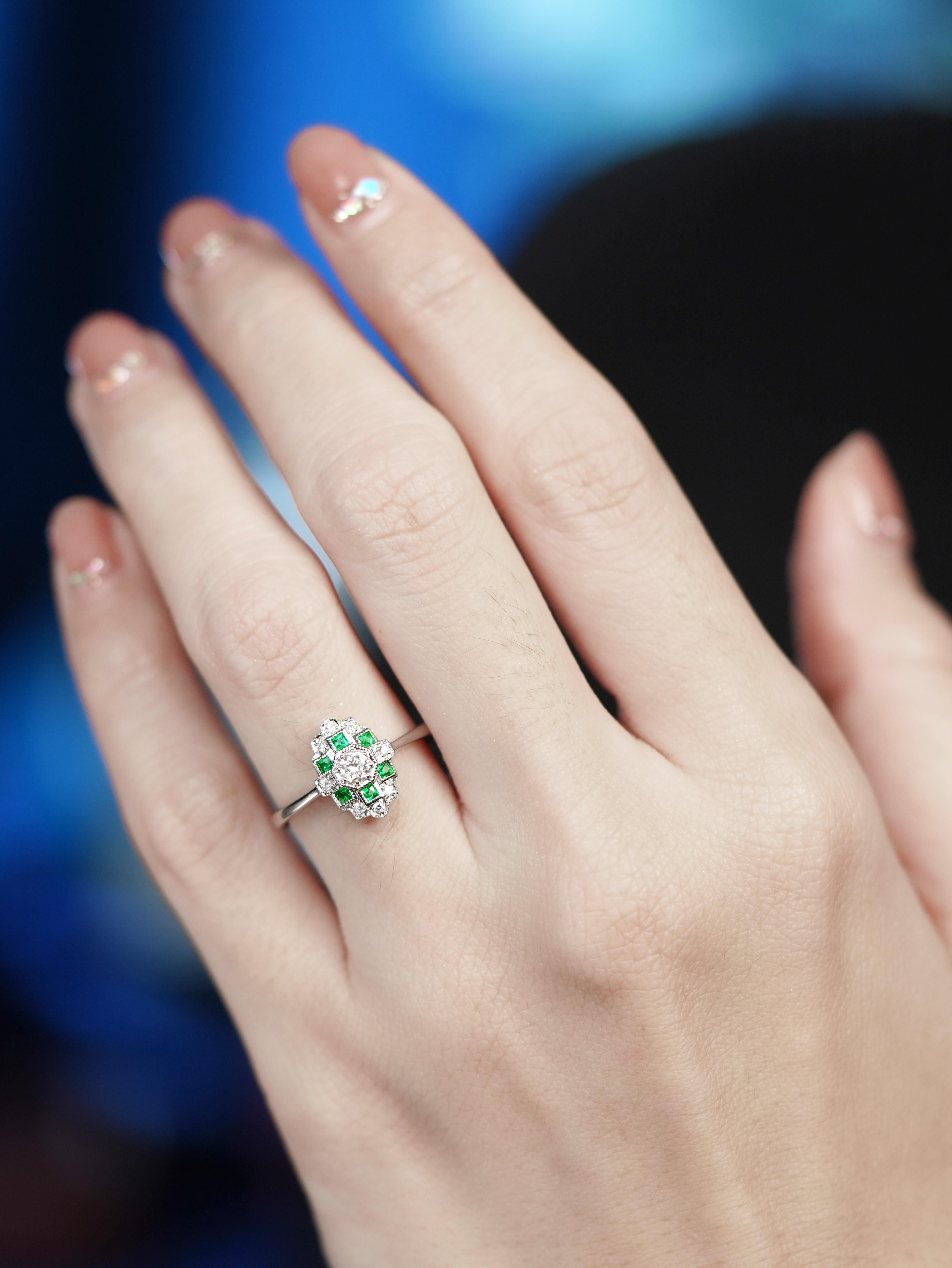 L'Art Déco rimane uno dei periodi preferiti da molti amanti dei gioielli dal design antico. Questo anello è un eccellente esempio del periodo. Il diamante centrale da circa 0,10 carati è circondato da sei smeraldi di forma quadrata e nove smeraldi