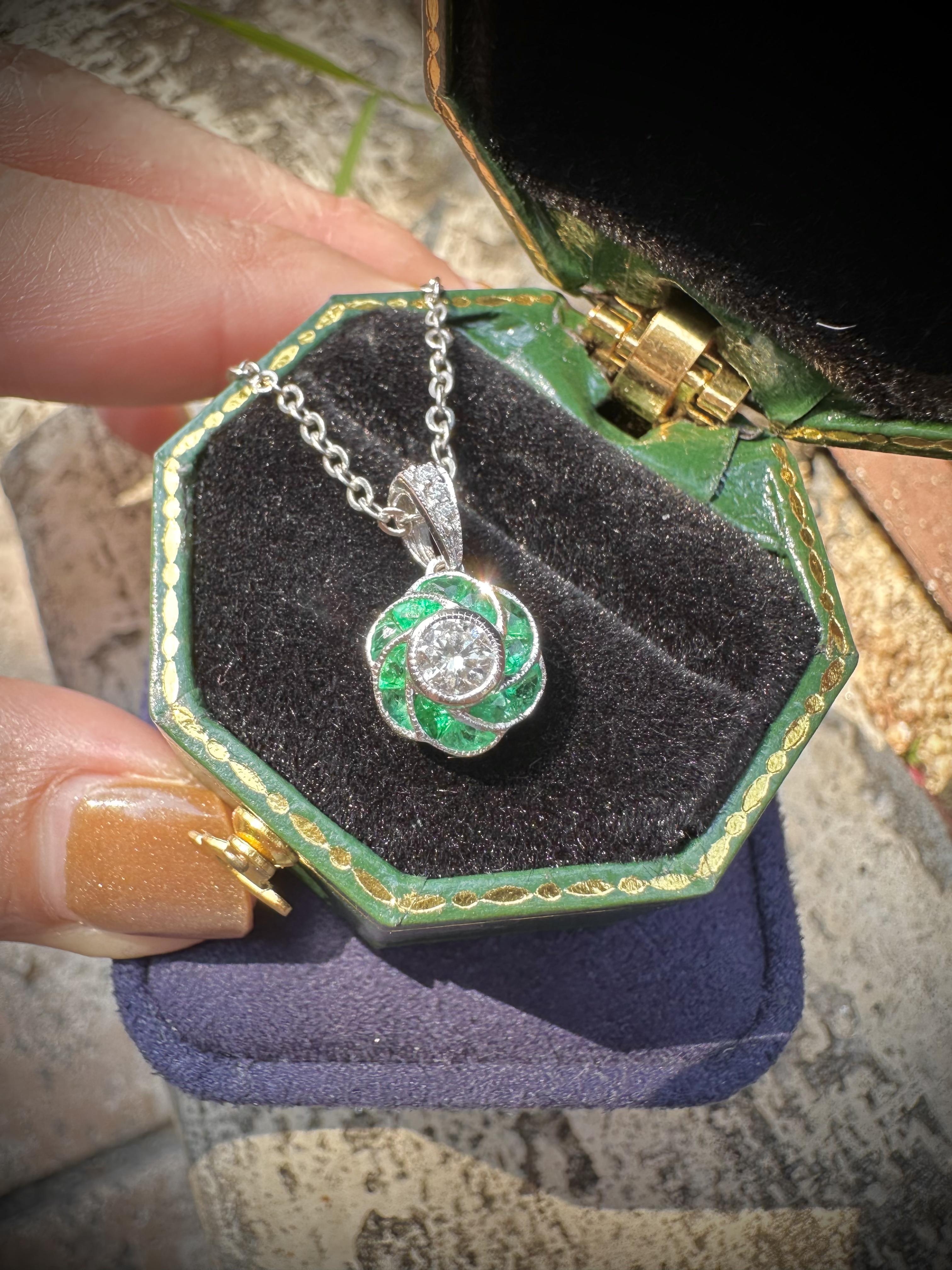 A luminous round diamond glows at the center, embraced by a vivid frame of French-cut emeralds in a graceful rose flower motif. Echoing the elegance of the Art Deco era, each emerald petal is precision-cut, radiating symmetry and vintage charm. This