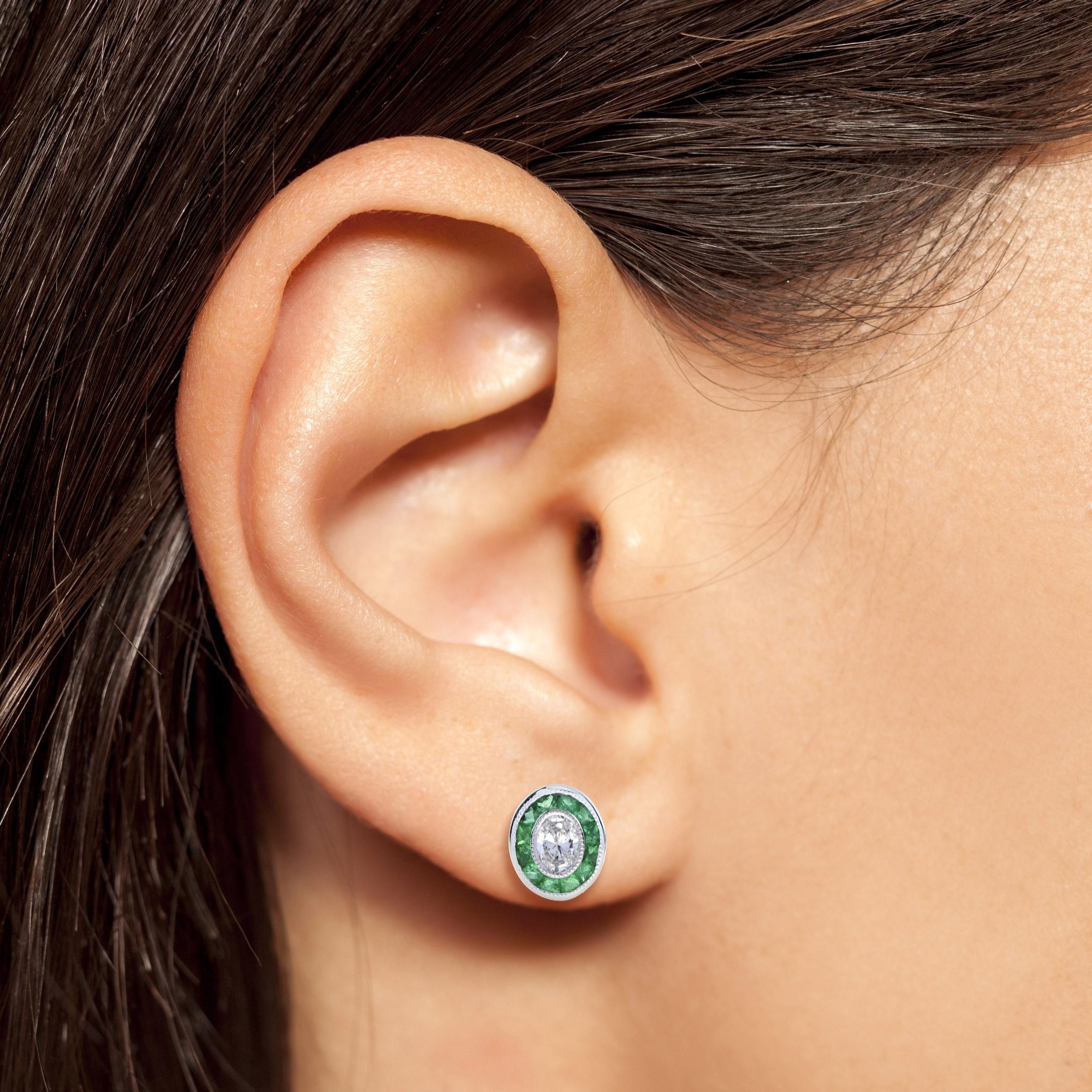 These Art-Deco stud earrings are completely spectacular! The vibrant green emerald is a specialty cut to surround the excellent oval cut center diamond, which is in a thin bezel with millgrain detail. Crafted in 18k white gold.

Earrings
