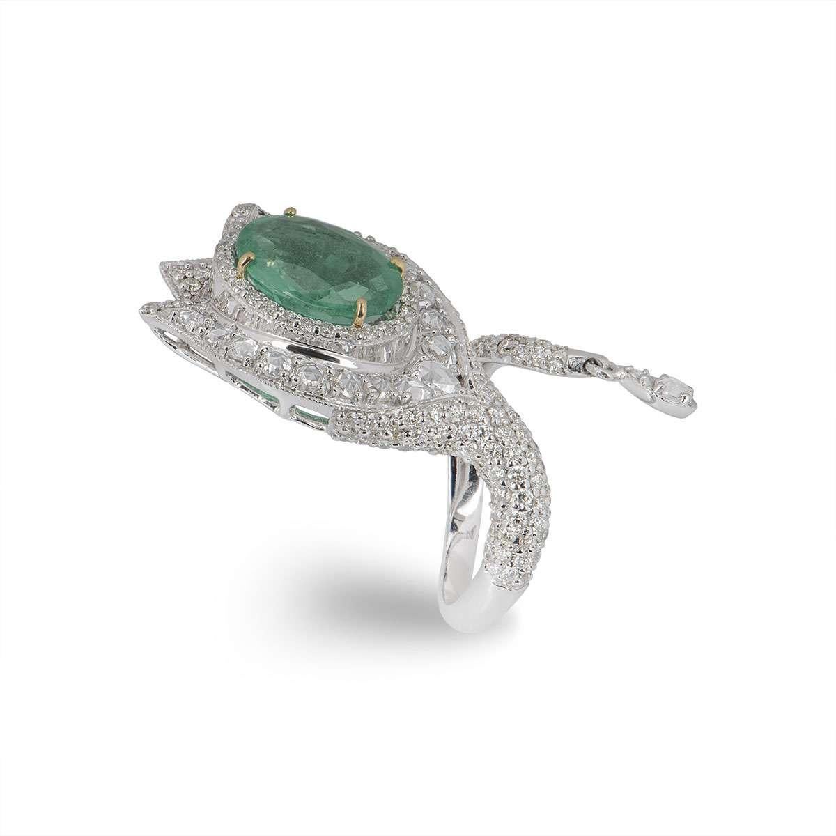An 18k white gold diamond and emerald dress ring. The ring wraps around the finger and is set with round brilliant cut diamonds and rose cut diamonds. The ring is set to the centre with an oval cut emerald weighing 3.37ct, displaying an even bright